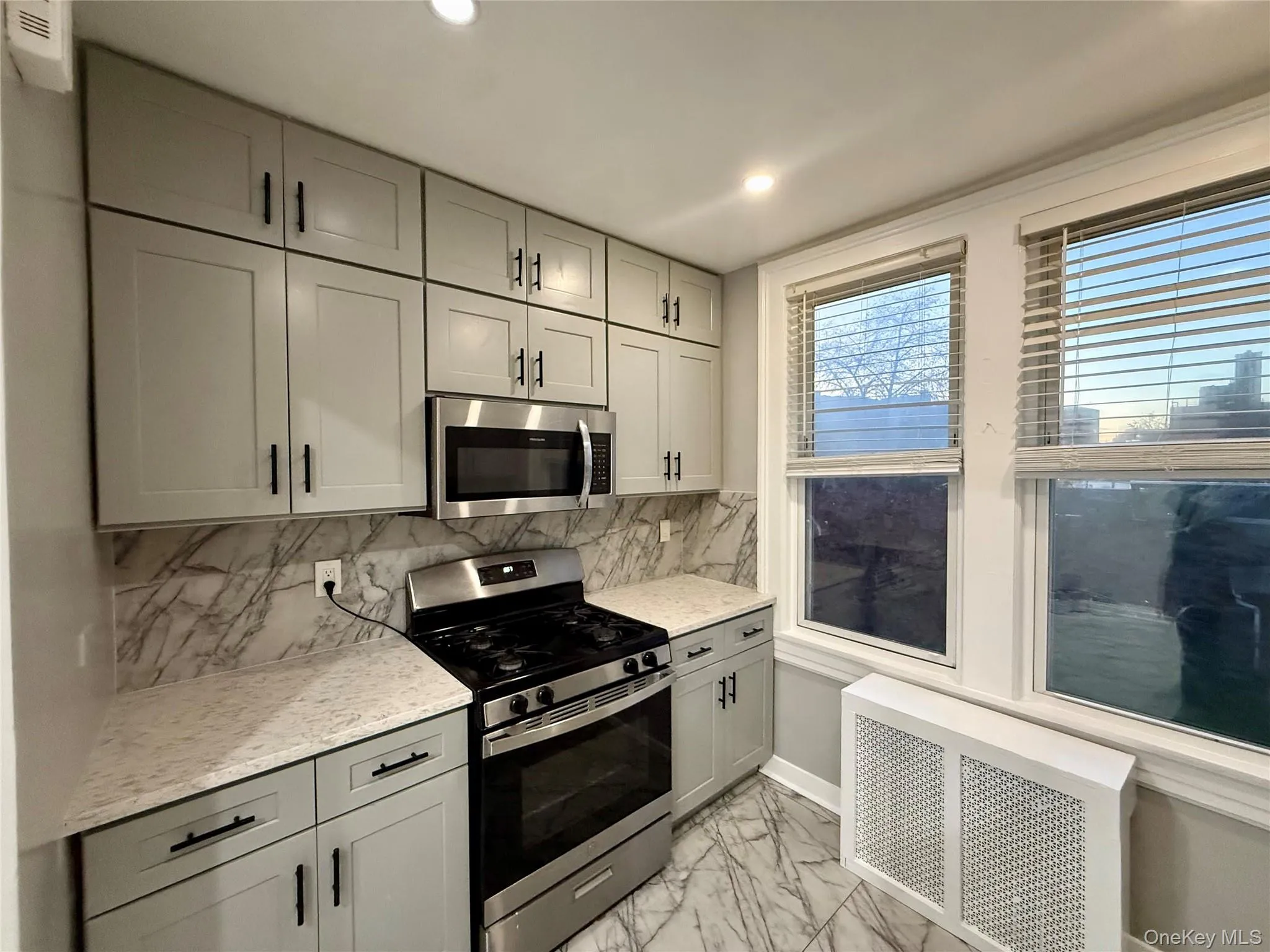 Kitchen featuring appliances with stainless steel finishes, radiator, gray cabinetry, tasteful backsplash, and light marble finish floors Kitchen featuring appliances with stainless steel finishes, radiator, gray cabinetry, tasteful backsplash, and light marble finish floors