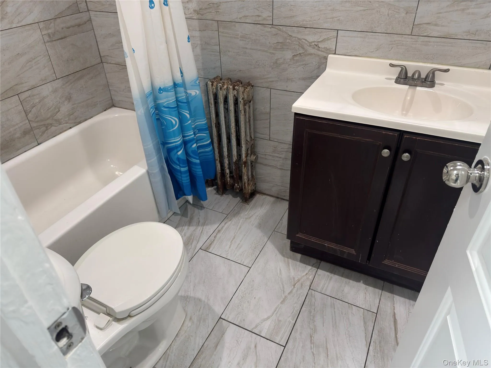 Bathroom with vanity, tile walls, radiator, and shower / bath combo Bathroom with vanity, tile walls, radiator, and shower / bath combo