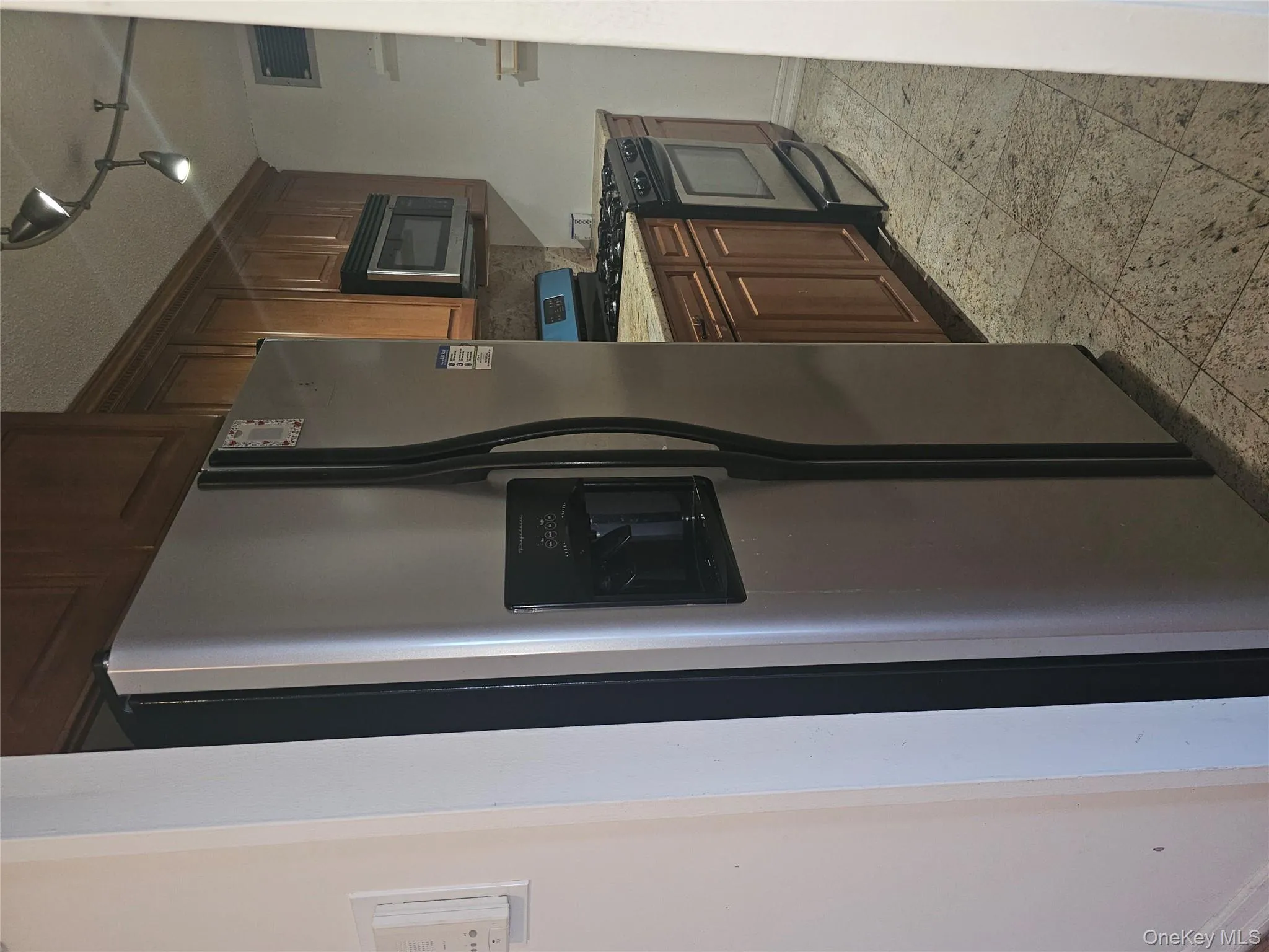 Kitchen with appliances with stainless steel finishes, track lighting, light stone counters, and backsplash Kitchen with appliances with stainless steel finishes, track lighting, light stone counters, and backsplash