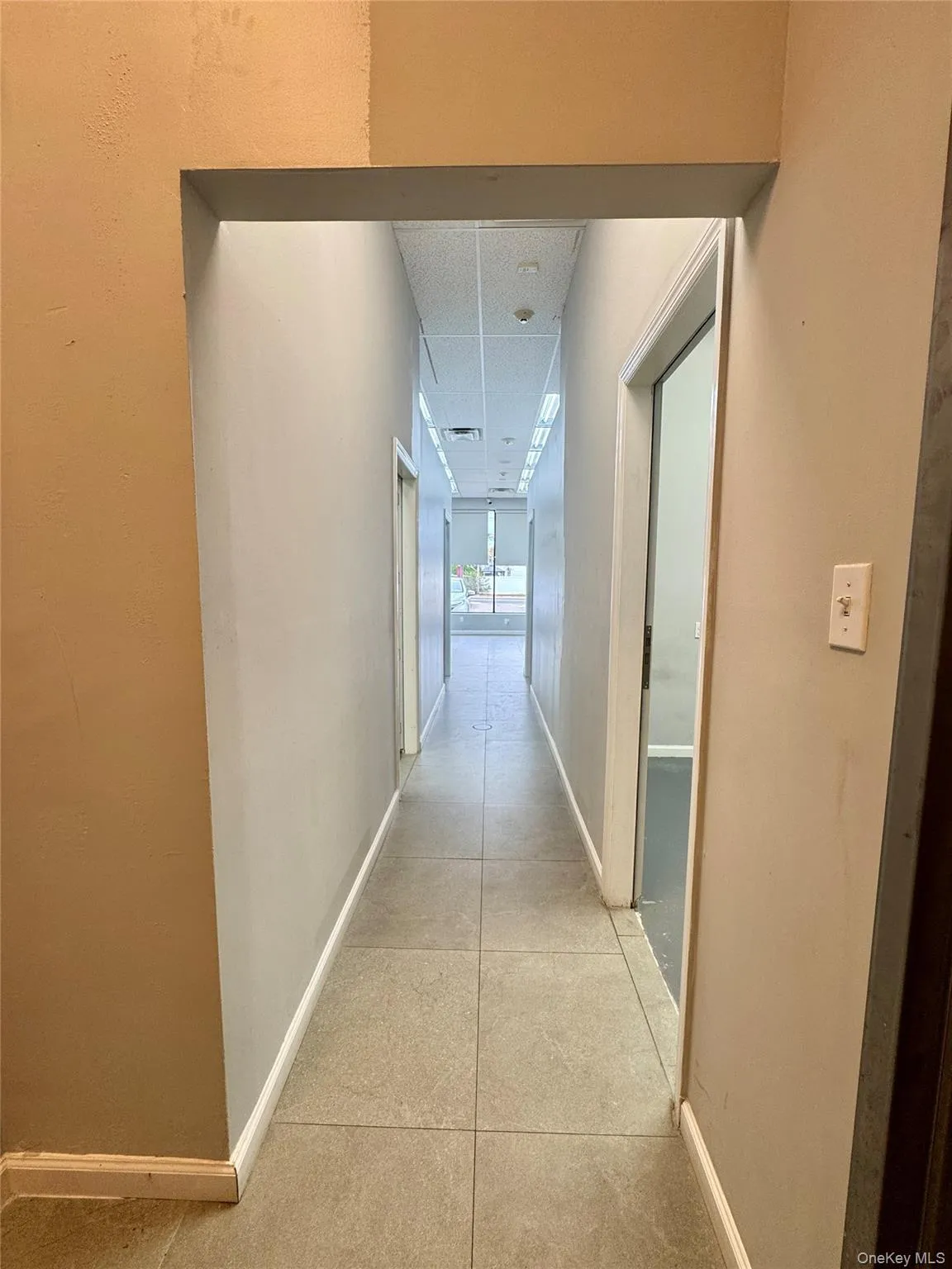 Hall featuring light tile patterned flooring and a drop ceiling Hall featuring light tile patterned flooring and a drop ceiling