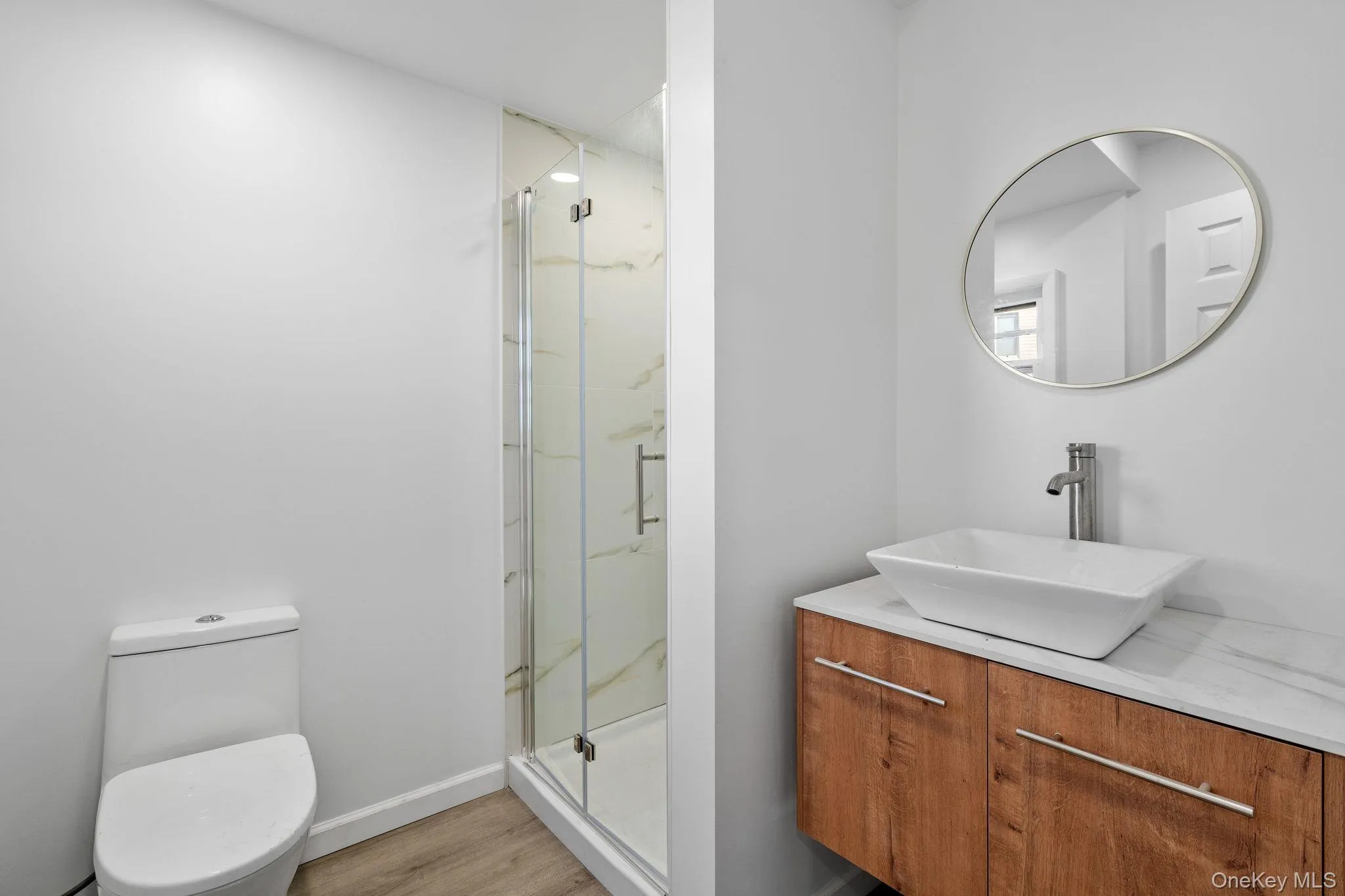 Bathroom featuring vanity, a marble finish shower, and light wood-style flooring Bathroom featuring vanity, a marble finish shower, and light wood-style flooring