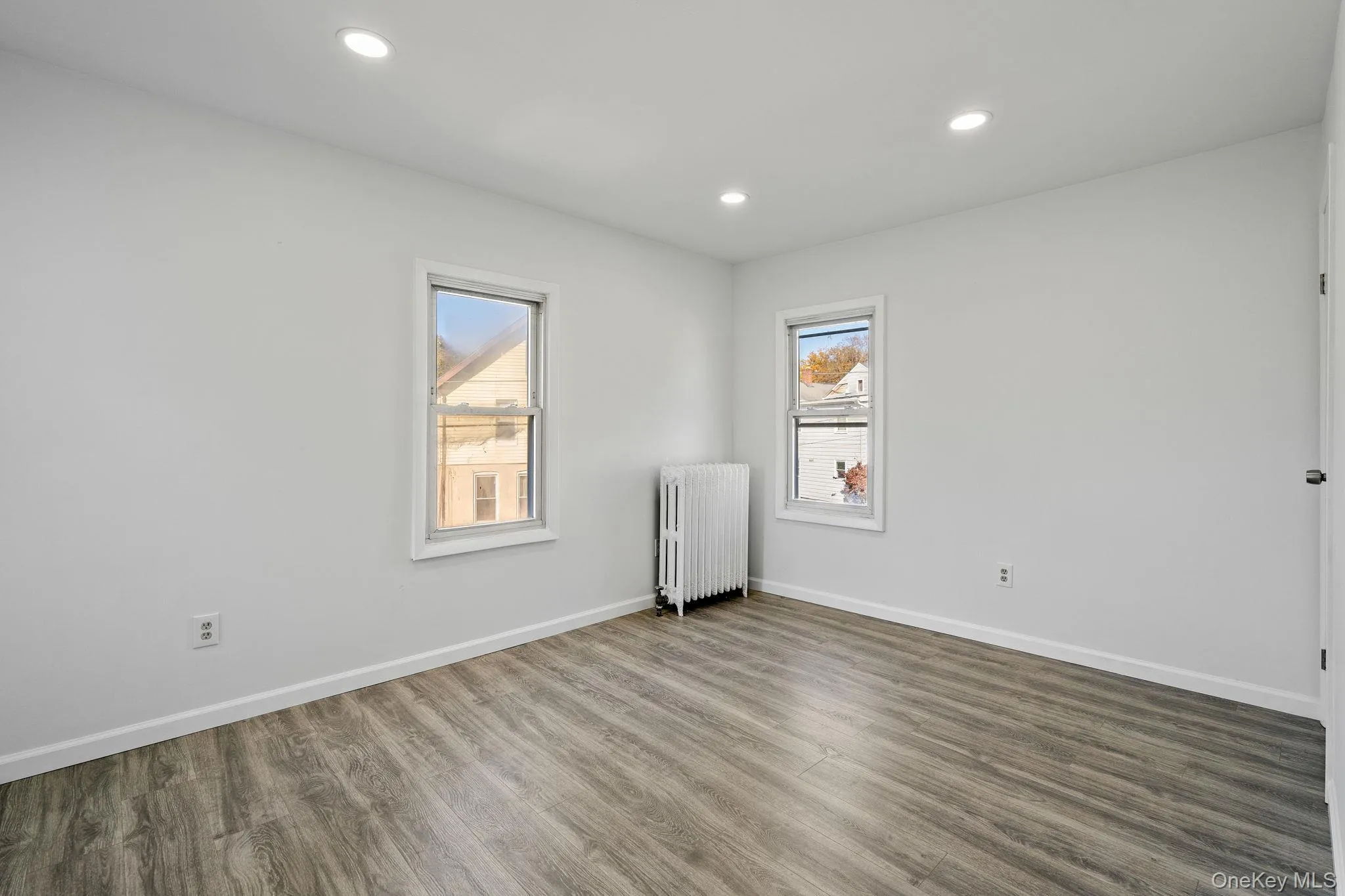 Empty room featuring wood finished floors, radiator heating unit, healthy amount of natural light, and recessed lighting Empty room featuring wood finished floors, radiator heating unit, healthy amount of natural light, and recessed lighting