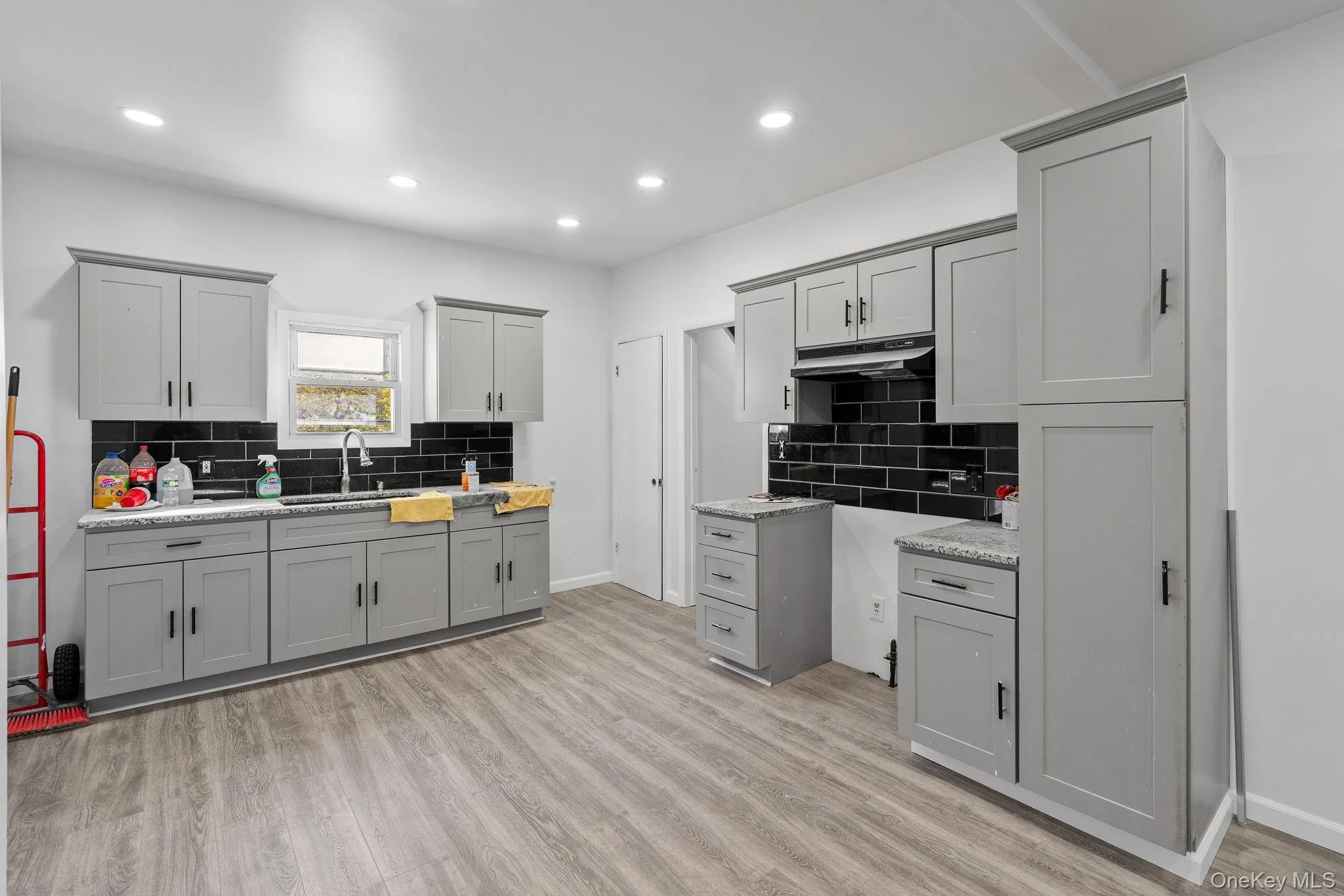 Kitchen with gray cabinetry, tasteful backsplash, recessed lighting, light wood-type flooring, and light stone counters Kitchen with gray cabinetry, tasteful backsplash, recessed lighting, light wood-type flooring, and light stone counters