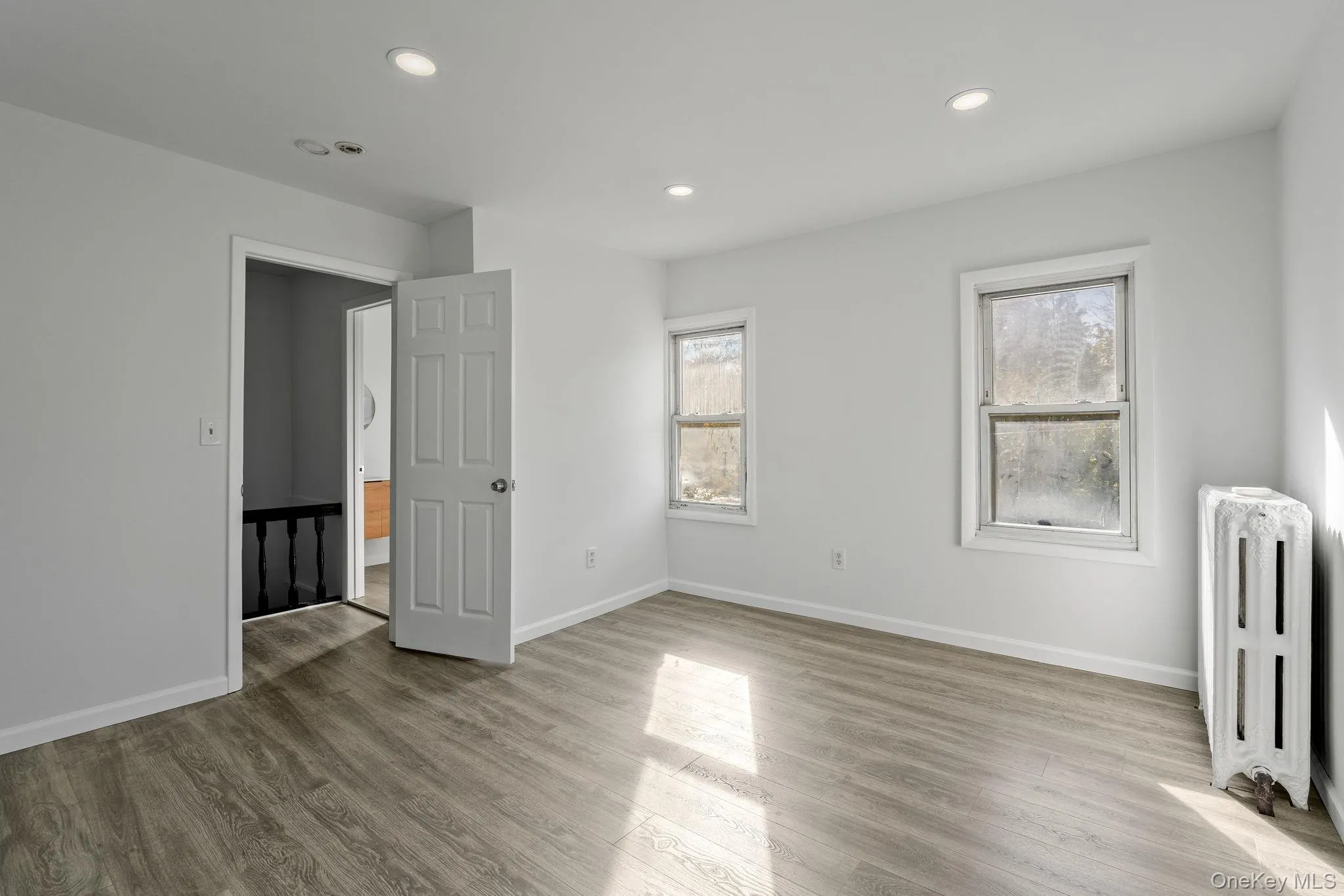 Unfurnished bedroom with radiator heating unit, light wood-style floors, multiple windows, and recessed lighting Unfurnished bedroom with radiator heating unit, light wood-style floors, multiple windows, and recessed lighting