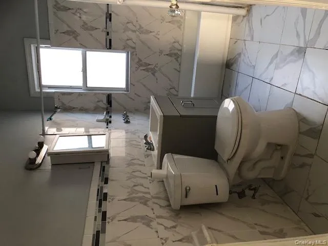 Bathroom featuring light marble finish floors, vanity, tile walls, and shower / tub combination Bathroom featuring light marble finish floors, vanity, tile walls, and shower / tub combination