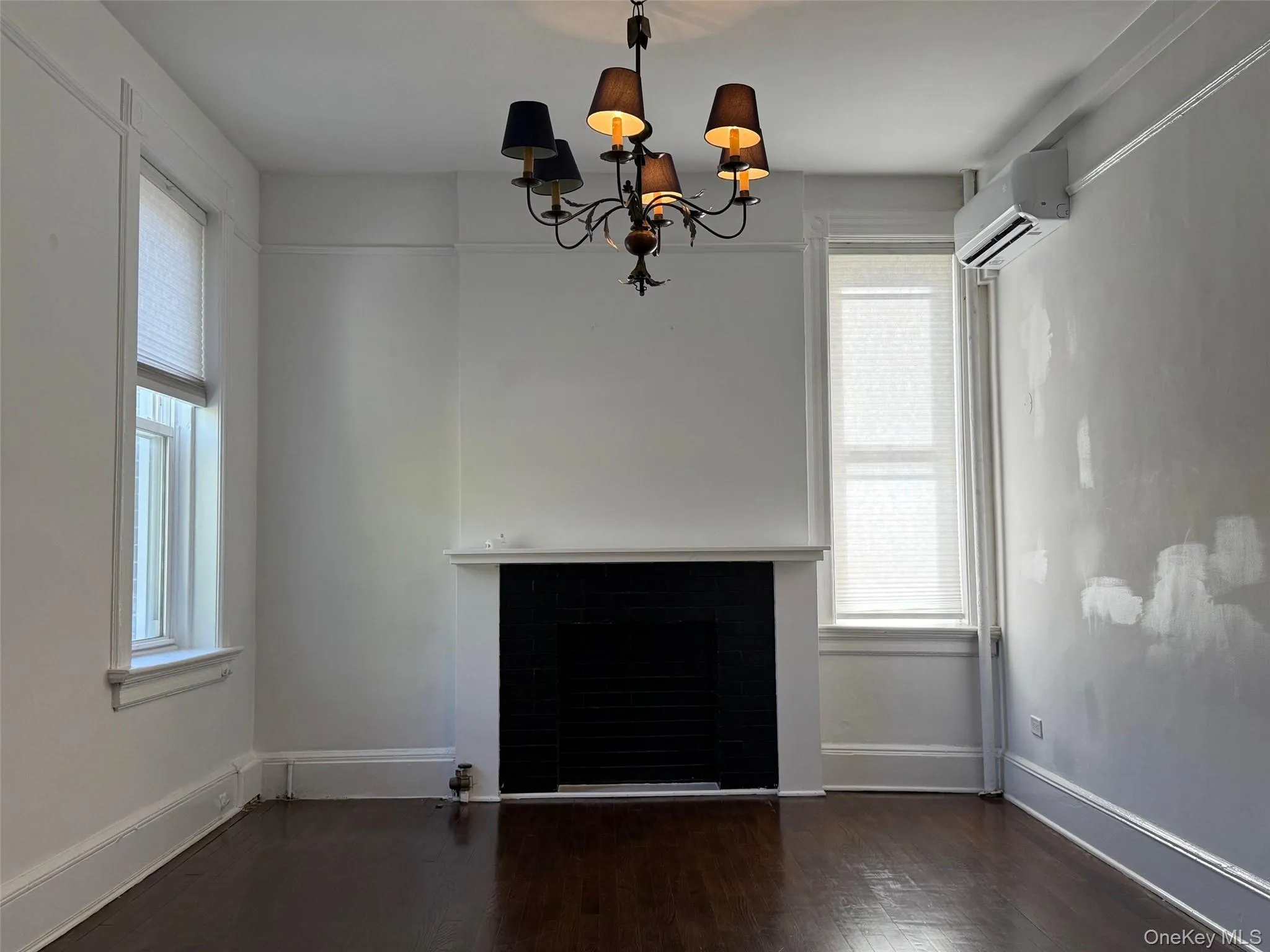 Unfurnished living room featuring dark wood-type flooring, a non-working fireplace, an AC wall unit, and a chandelier Unfurnished living room featuring dark wood-type flooring, a non-working fireplace, an AC wall unit, and a chandelier