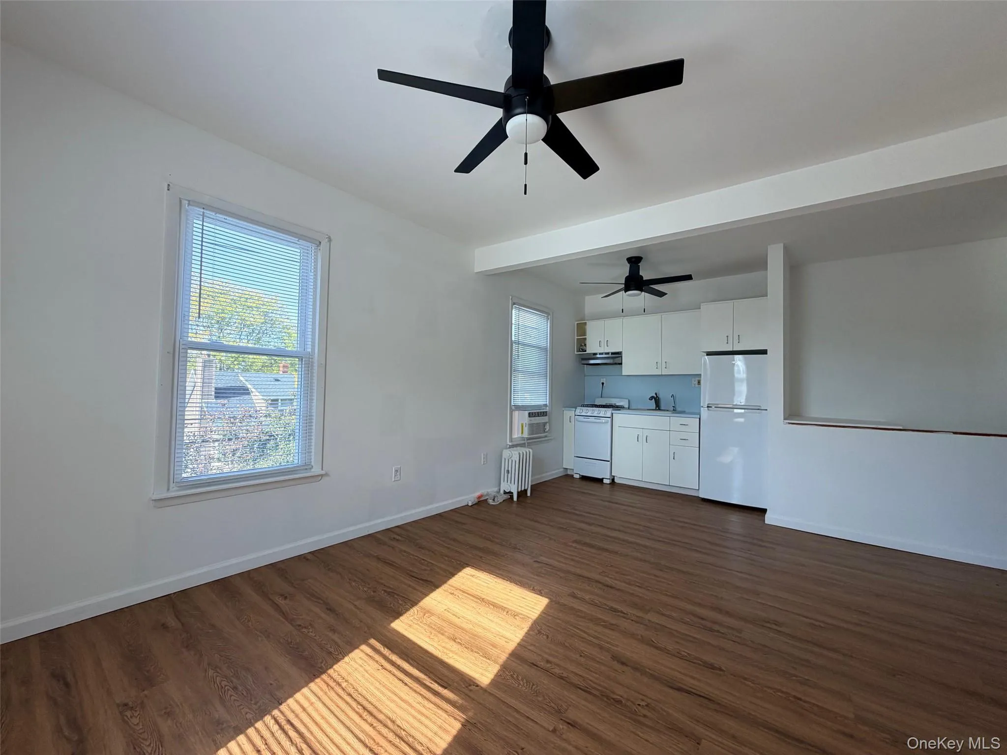 Unfurnished living room featuring dark wood-type flooring, radiator heating unit, beam ceiling, ceiling fan, and cooling unit Unfurnished living room featuring dark wood-type flooring, radiator heating unit, beam ceiling, ceiling fan, and cooling unit
