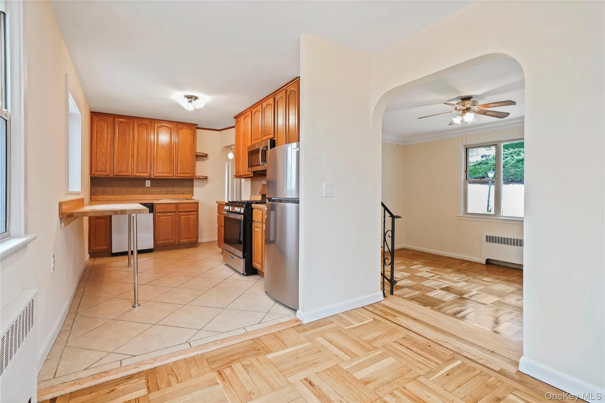 Kitchen featuring arched walkways, radiator heating unit, light countertops, ceiling fan, and stainless steel appliances Kitchen featuring arched walkways, radiator heating unit, light countertops, ceiling fan, and stainless steel appliances