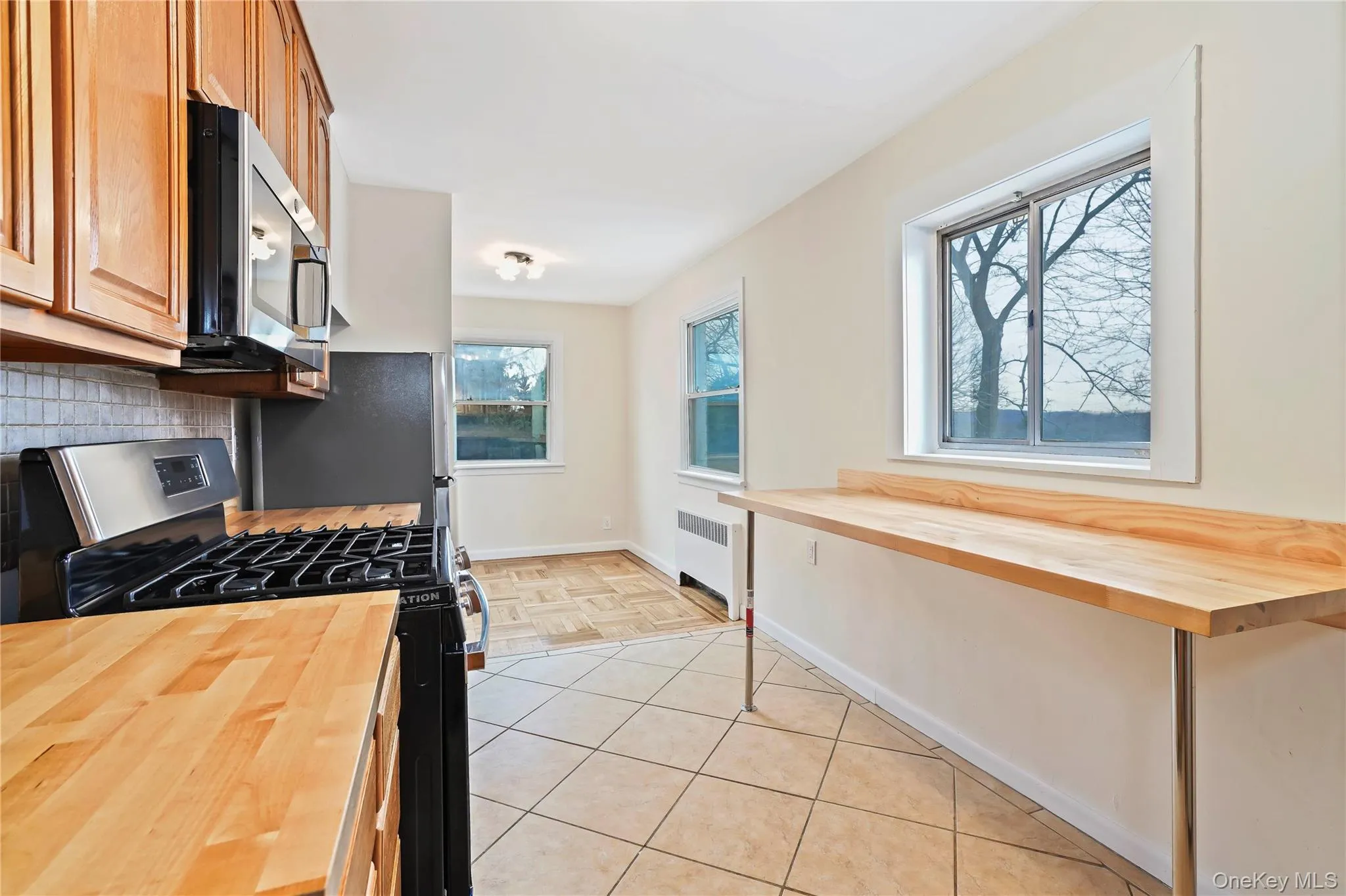 Kitchen featuring wooden counters, appliances with stainless steel finishes, radiator, tasteful backsplash, and light tile patterned flooring Kitchen featuring wooden counters, appliances with stainless steel finishes, radiator, tasteful backsplash, and light tile patterned flooring