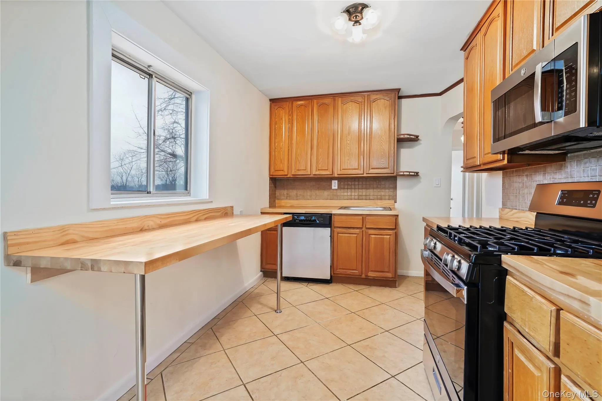 Kitchen featuring appliances with stainless steel finishes, butcher block countertops, tasteful backsplash, light tile patterned floors, and arched walkways Kitchen featuring appliances with stainless steel finishes, butcher block countertops, tasteful backsplash, light tile patterned floors, and arched walkways