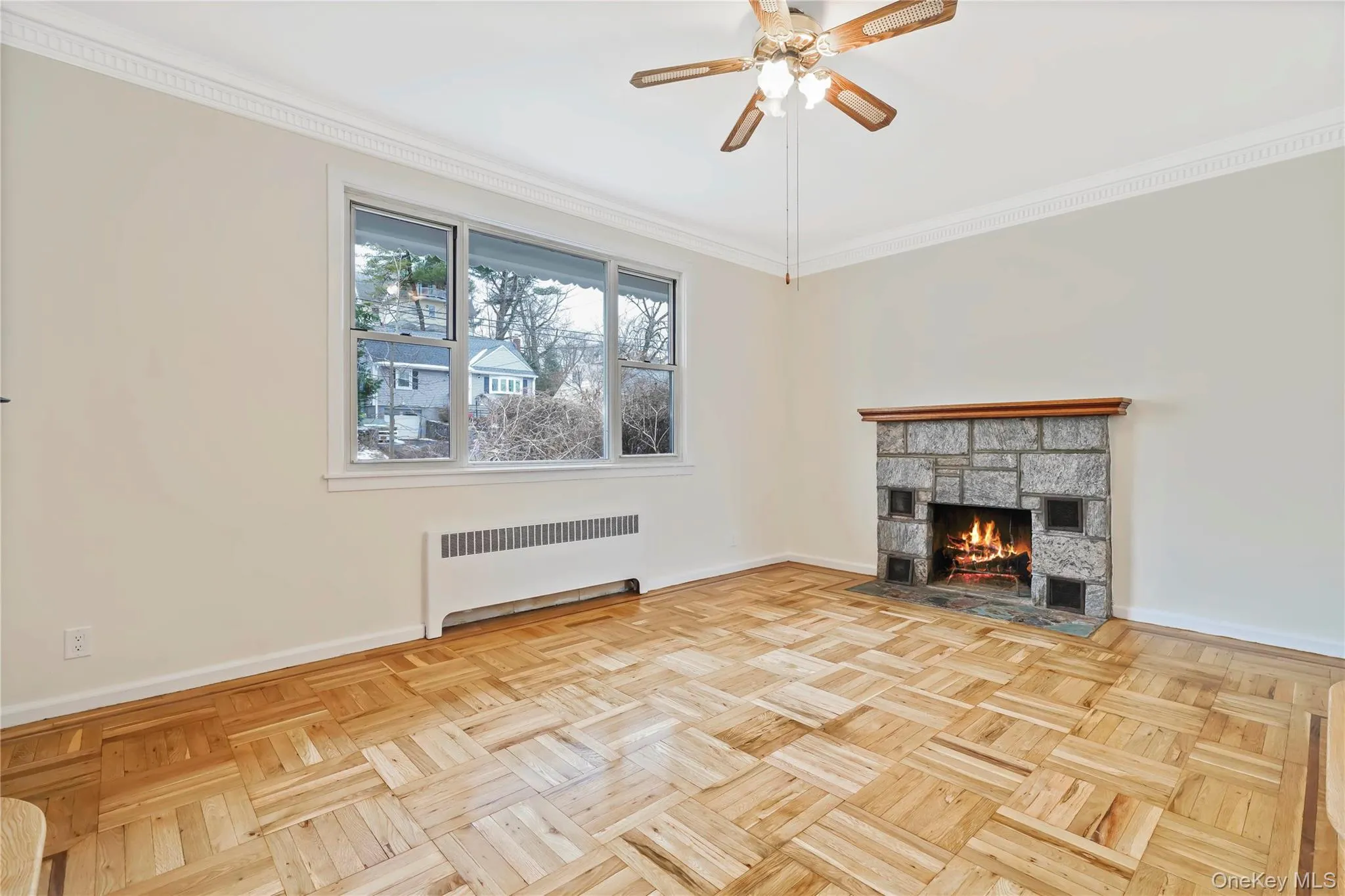 Unfurnished living room featuring crown molding, radiator heating unit, a stone fireplace, and a ceiling fan Unfurnished living room featuring crown molding, radiator heating unit, a stone fireplace, and a ceiling fan