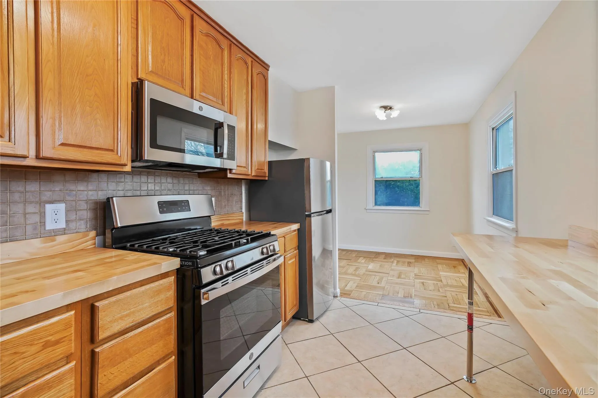 Kitchen featuring wooden counters, appliances with stainless steel finishes, decorative backsplash, brown cabinetry, and light tile patterned floors Kitchen featuring wooden counters, appliances with stainless steel finishes, decorative backsplash, brown cabinetry, and light tile patterned floors