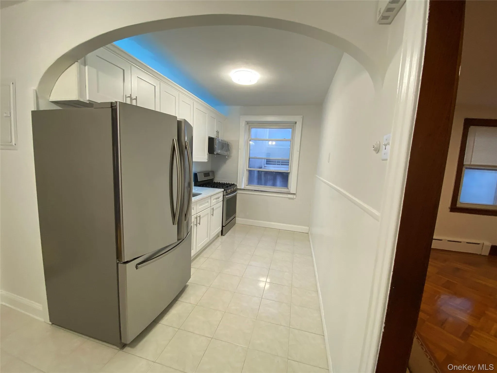 Kitchen with stainless steel appliances, white cabinetry, arched walkways, a baseboard heating unit, and light tile patterned flooring Kitchen with stainless steel appliances, white cabinetry, arched walkways, a baseboard heating unit, and light tile patterned flooring