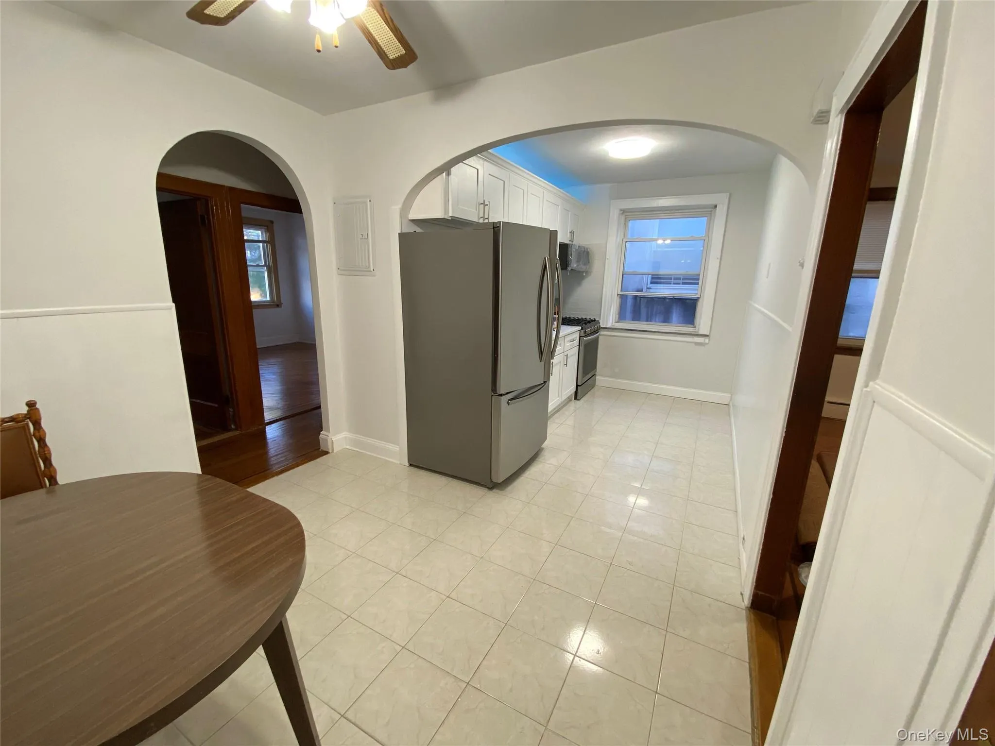Kitchen featuring arched walkways, stainless steel appliances, white cabinetry, ceiling fan, and light tile patterned flooring Kitchen featuring arched walkways, stainless steel appliances, white cabinetry, ceiling fan, and light tile patterned flooring