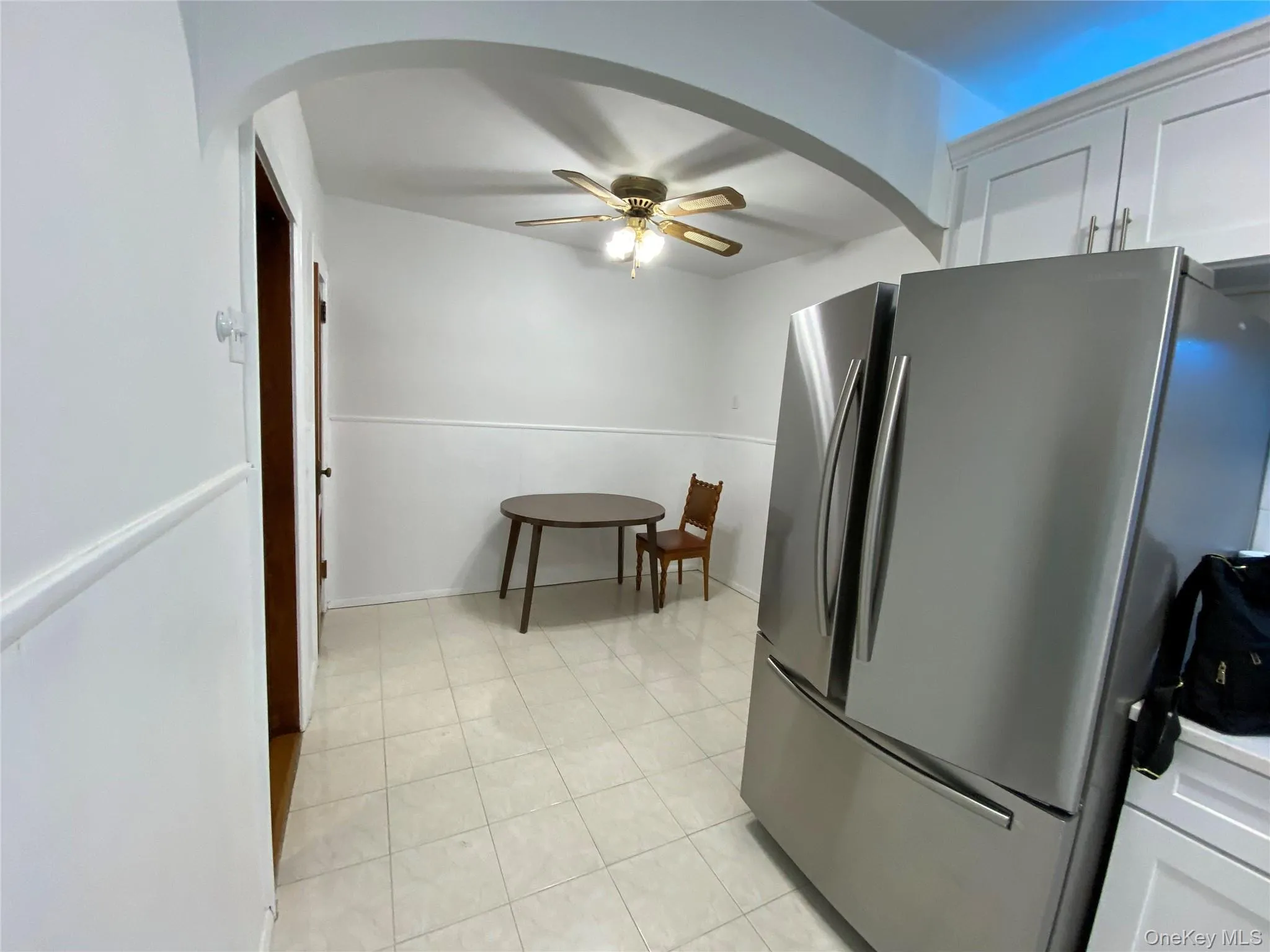 Kitchen featuring freestanding refrigerator, arched walkways, ceiling fan, white cabinets, and light tile patterned flooring Kitchen featuring freestanding refrigerator, arched walkways, ceiling fan, white cabinets, and light tile patterned flooring