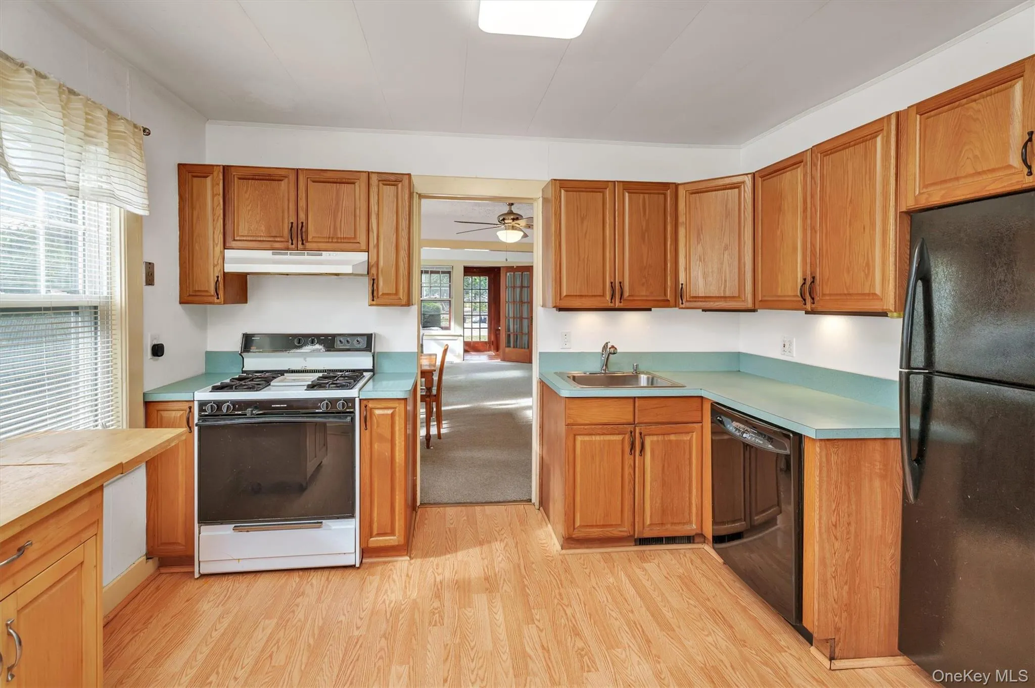 Kitchen featuring black appliances, light wood-style floors, under cabinet range hood, brown cabinetry, and a ceiling fan Kitchen featuring black appliances, light wood-style floors, under cabinet range hood, brown cabinetry, and a ceiling fan