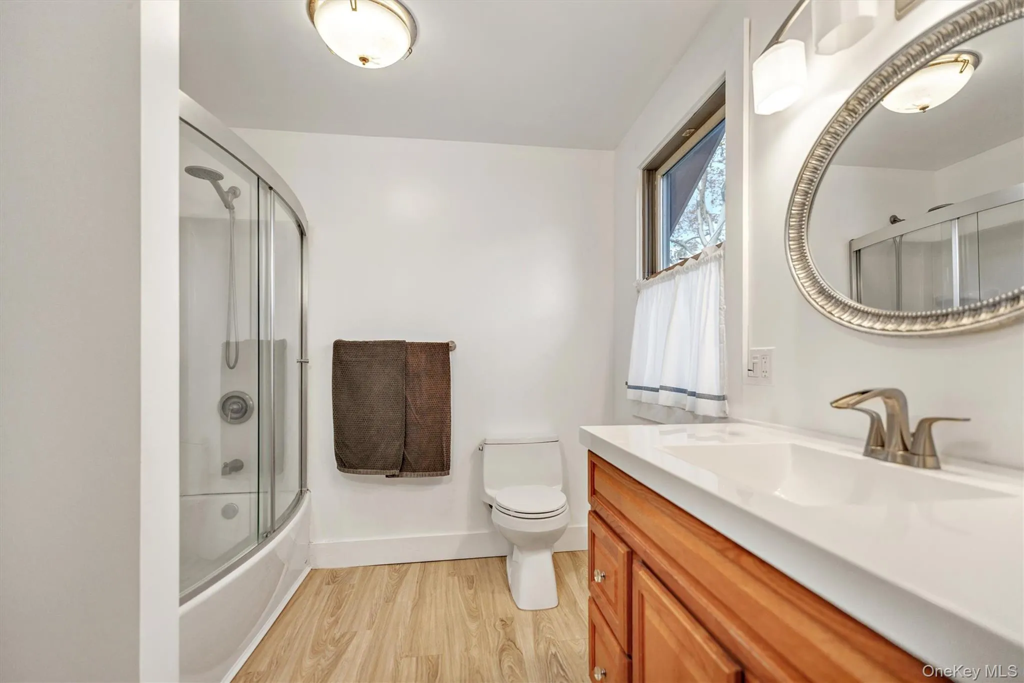 Bathroom featuring light wood finished floors, vanity, and enclosed tub / shower combo Bathroom featuring light wood finished floors, vanity, and enclosed tub / shower combo