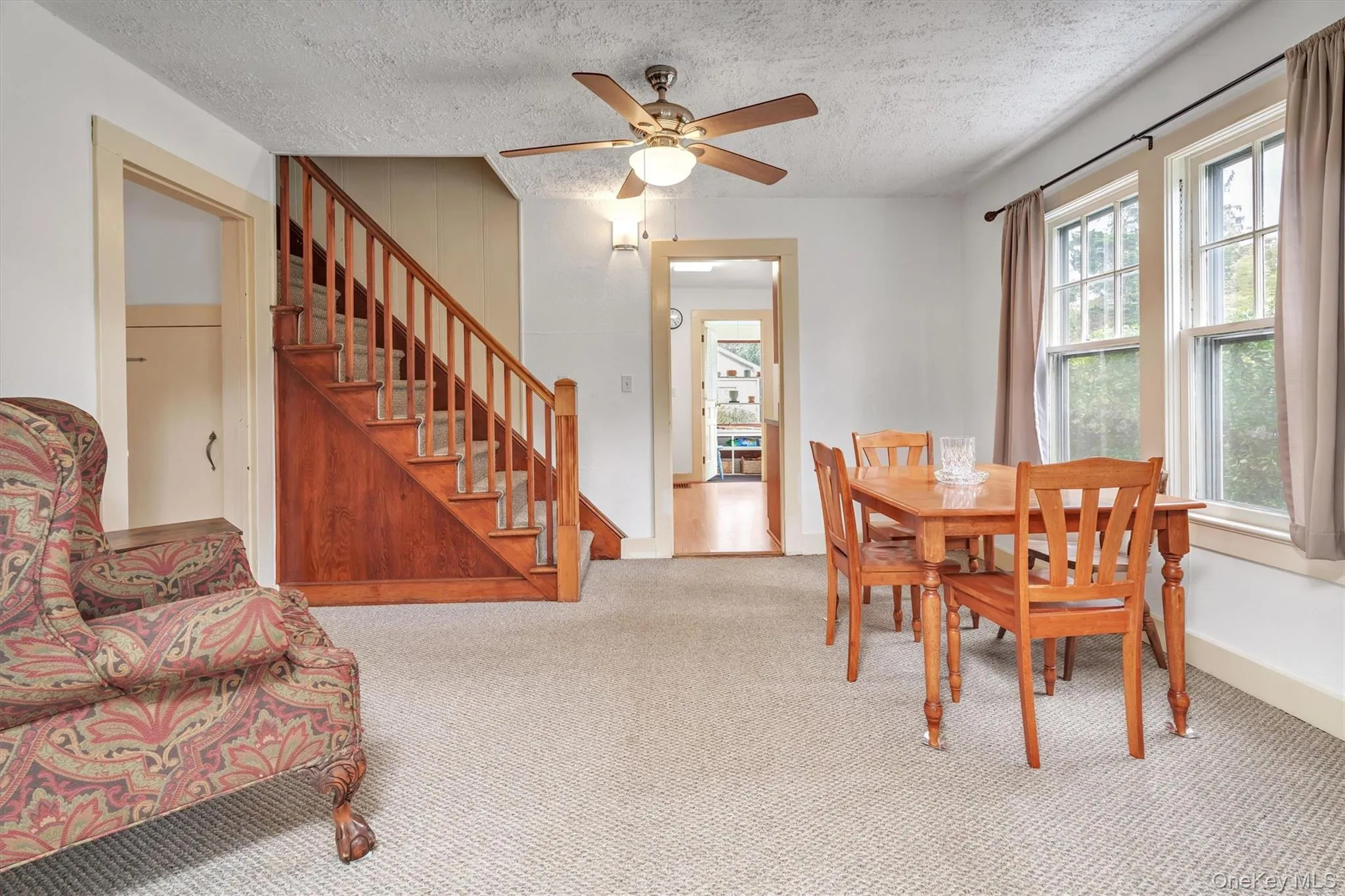Carpeted dining space featuring a textured ceiling, a ceiling fan, and stairway Carpeted dining space featuring a textured ceiling, a ceiling fan, and stairway