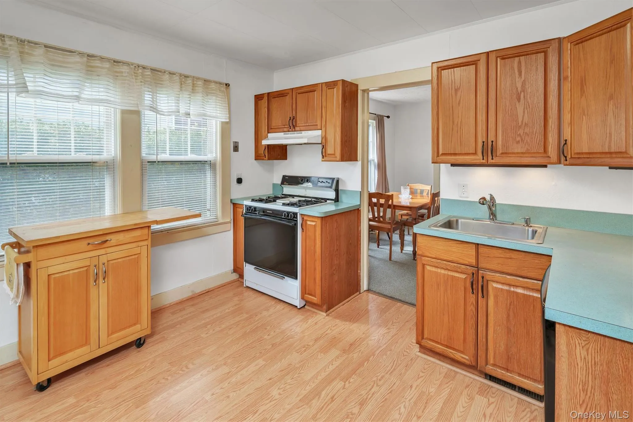 Kitchen featuring range with gas cooktop, light countertops, light wood-style floors, and under cabinet range hood Kitchen featuring range with gas cooktop, light countertops, light wood-style floors, and under cabinet range hood
