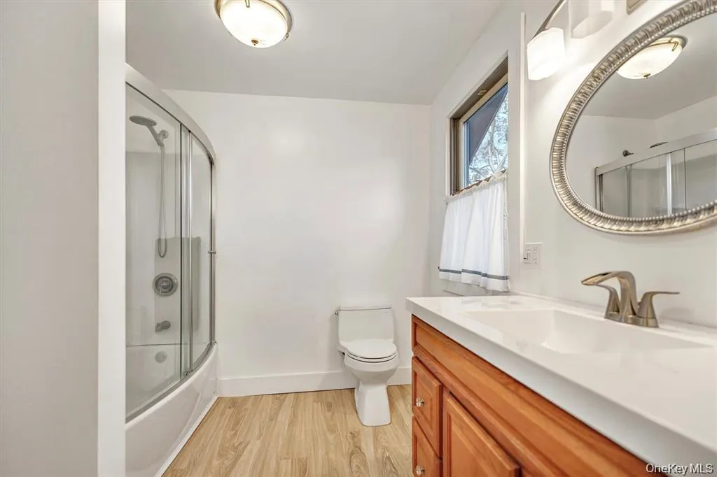 Full bathroom featuring light wood finished floors, vanity, and bath / shower combo with glass door Full bathroom featuring light wood finished floors, vanity, and bath / shower combo with glass door