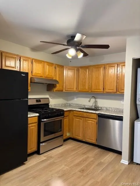 Kitchen featuring stainless steel appliances, light wood-style floors, ceiling fan, under cabinet range hood, and stacked washer and clothes dryer Kitchen featuring stainless steel appliances, light wood-style floors, ceiling fan, under cabinet range hood, and stacked washer and clothes dryer