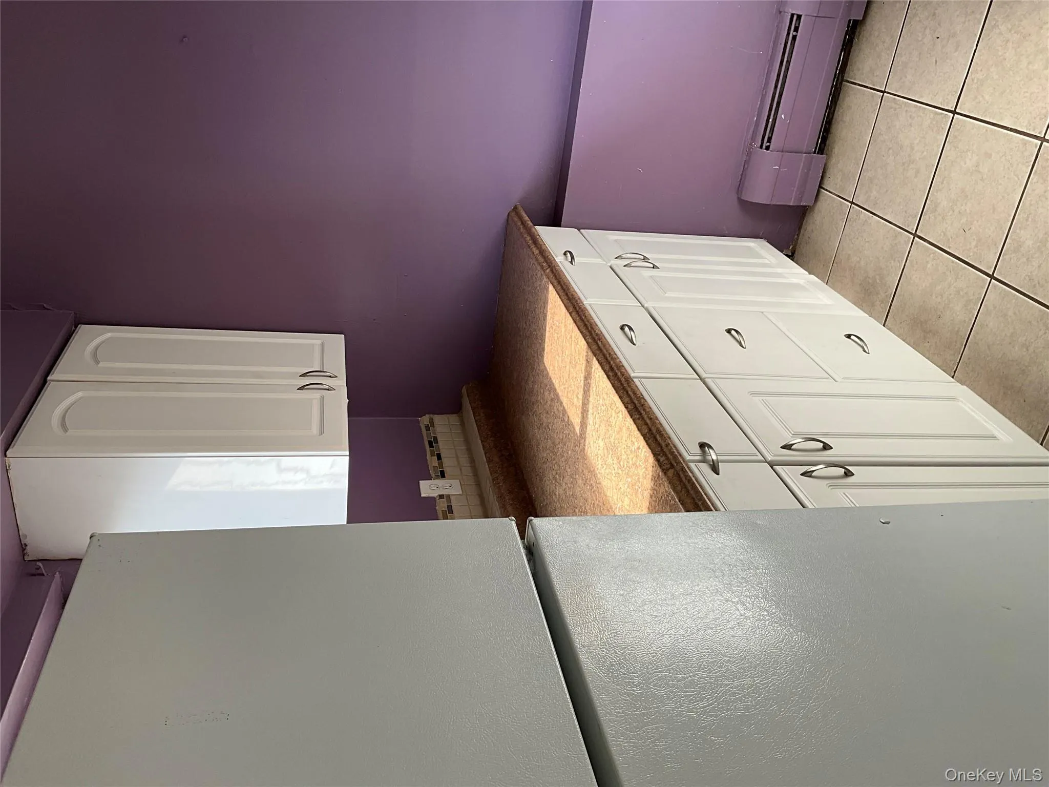 Kitchen featuring refrigerator, white cabinets, a baseboard heating unit, dark countertops, and light tile patterned flooring Kitchen featuring refrigerator, white cabinets, a baseboard heating unit, dark countertops, and light tile patterned flooring