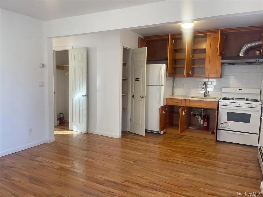 Kitchen with light countertops, white appliances, brown cabinetry, and open shelves Kitchen with light countertops, white appliances, brown cabinetry, and open shelves