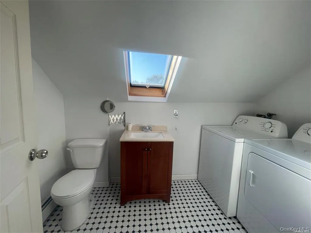 Bathroom with a skylight, vanity, separate washer and dryer, baseboard heating, and vaulted ceiling Bathroom with a skylight, vanity, separate washer and dryer, baseboard heating, and vaulted ceiling