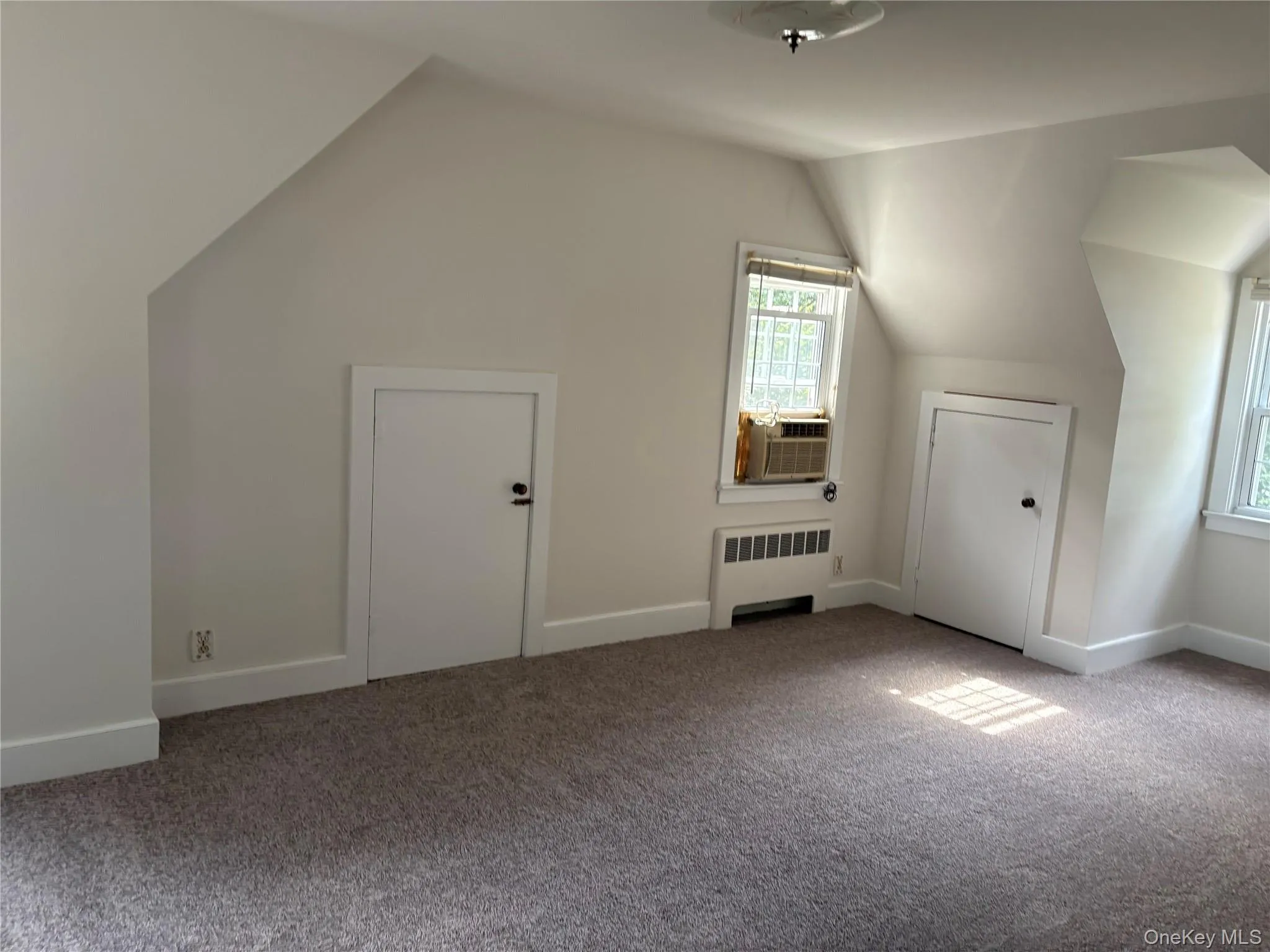 Additional living space featuring vaulted ceiling, radiator, carpet floors, and cooling unit Additional living space featuring vaulted ceiling, radiator, carpet floors, and cooling unit