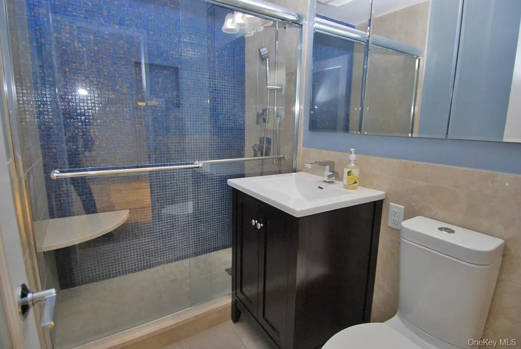 Full bathroom with a shower stall, vanity, tile walls, and light tile patterned flooring Full bathroom with a shower stall, vanity, tile walls, and light tile patterned flooring