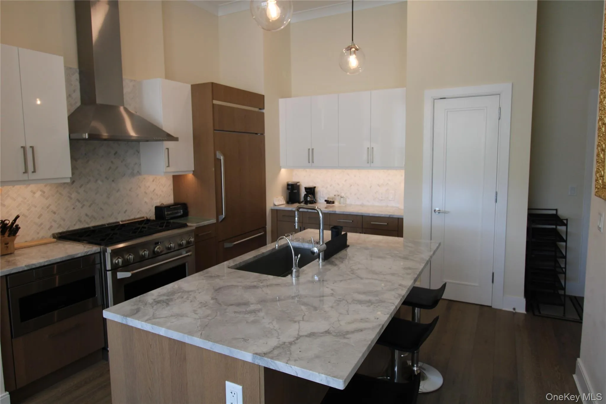 Kitchen with wall chimney exhaust hood, white cabinets, decorative backsplash, dark wood-style floors, and crown molding Kitchen with wall chimney exhaust hood, white cabinets, decorative backsplash, dark wood-style floors, and crown molding