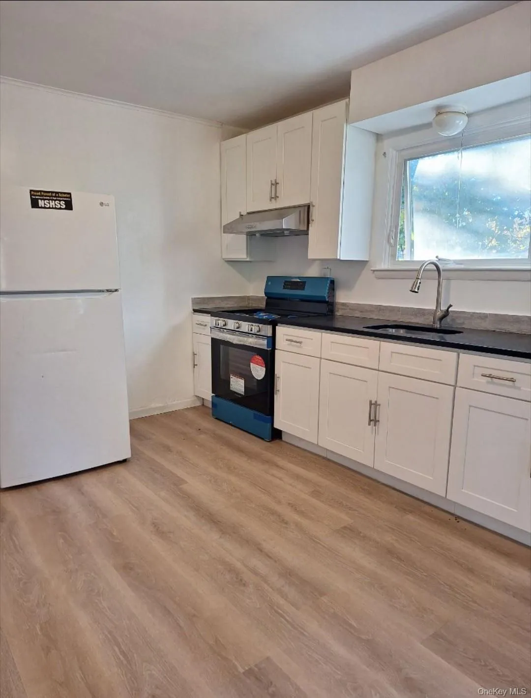 Kitchen featuring freestanding refrigerator, dark countertops, stainless steel gas range, white cabinets, and light wood finished floors Kitchen featuring freestanding refrigerator, dark countertops, stainless steel gas range, white cabinets, and light wood finished floors