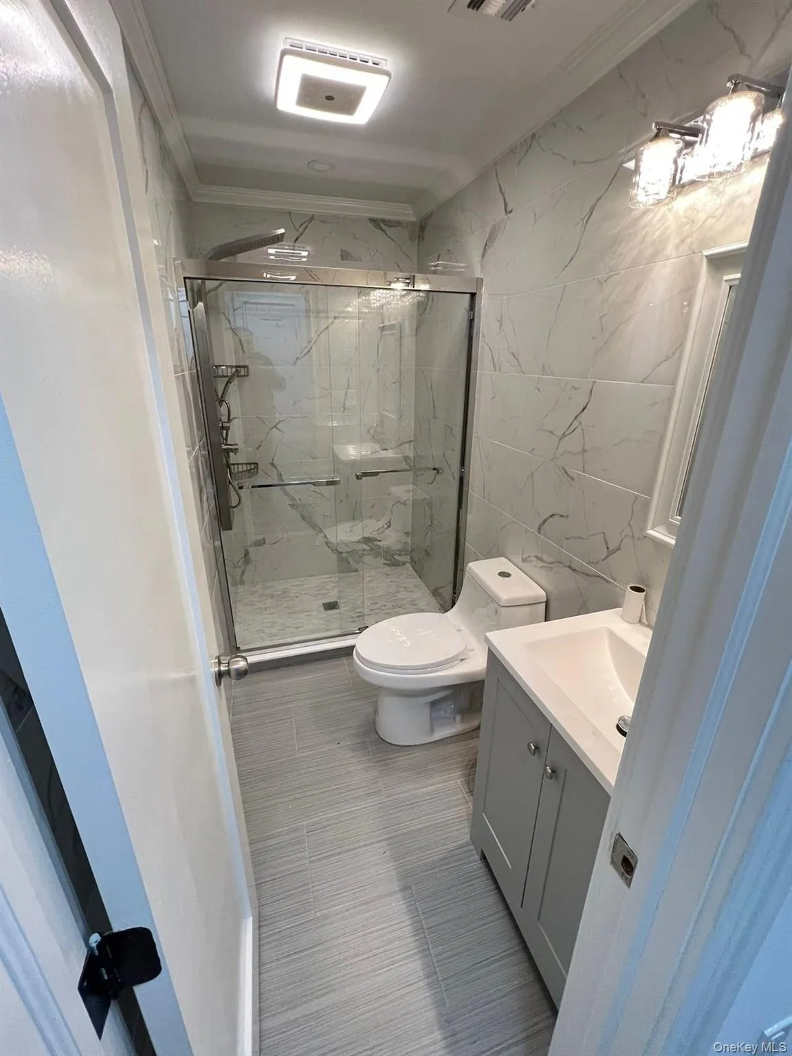 Full bath featuring tile walls, vanity, ornamental molding, and a marble finish shower Full bath featuring tile walls, vanity, ornamental molding, and a marble finish shower