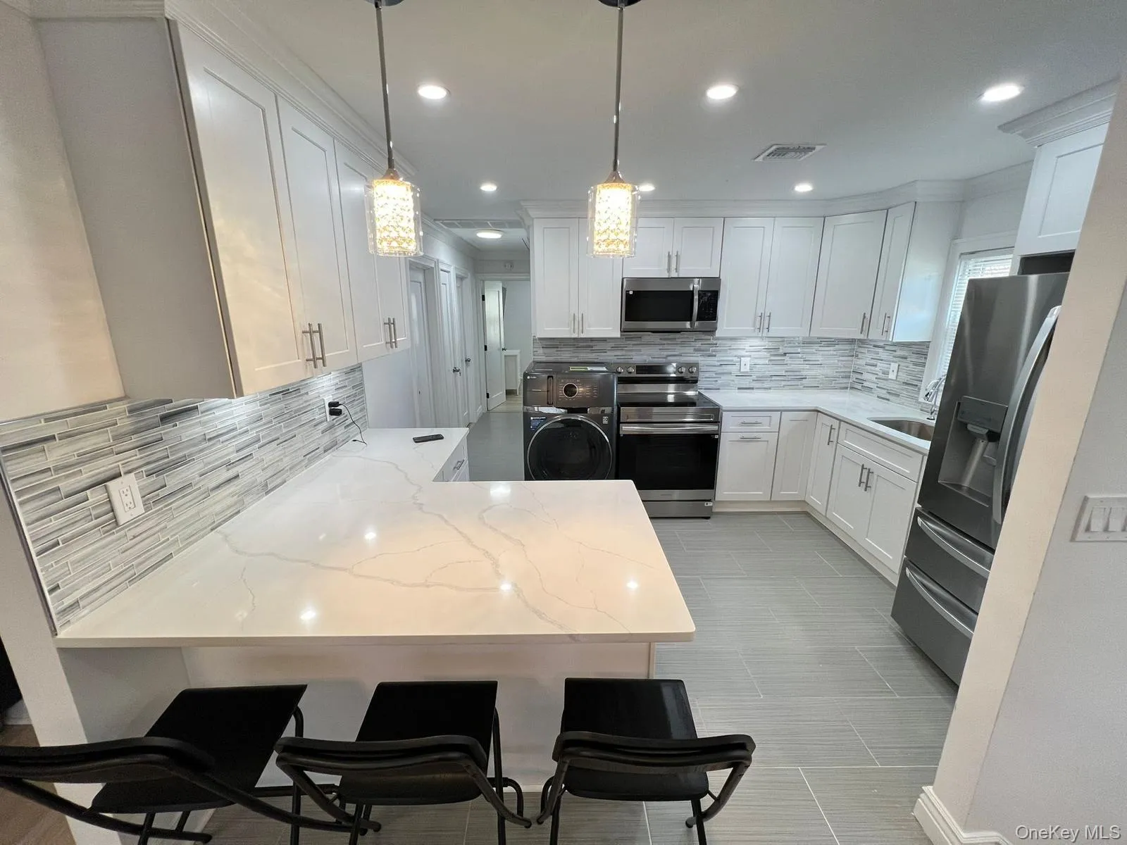 Kitchen with tasteful backsplash, stainless steel appliances, light stone countertops, a peninsula, and washer / clothes dryer Kitchen with tasteful backsplash, stainless steel appliances, light stone countertops, a peninsula, and washer / clothes dryer