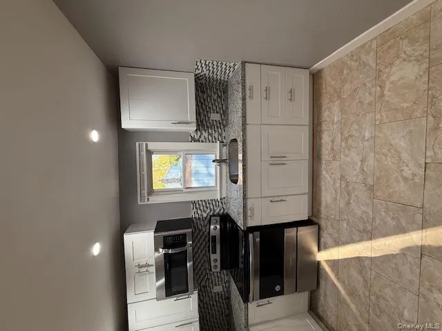 Kitchen with tasteful backsplash, stove, white cabinets, light stone counters, and recessed lighting Kitchen with tasteful backsplash, stove, white cabinets, light stone counters, and recessed lighting