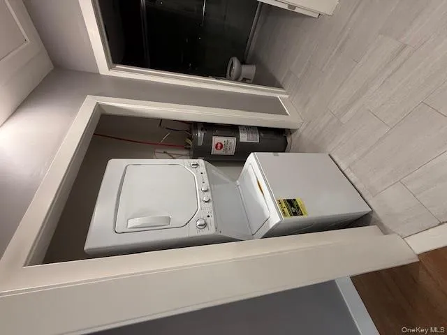 Laundry area with light wood-style floors, stacked washer and clothes dryer, and water heater Laundry area with light wood-style floors, stacked washer and clothes dryer, and water heater