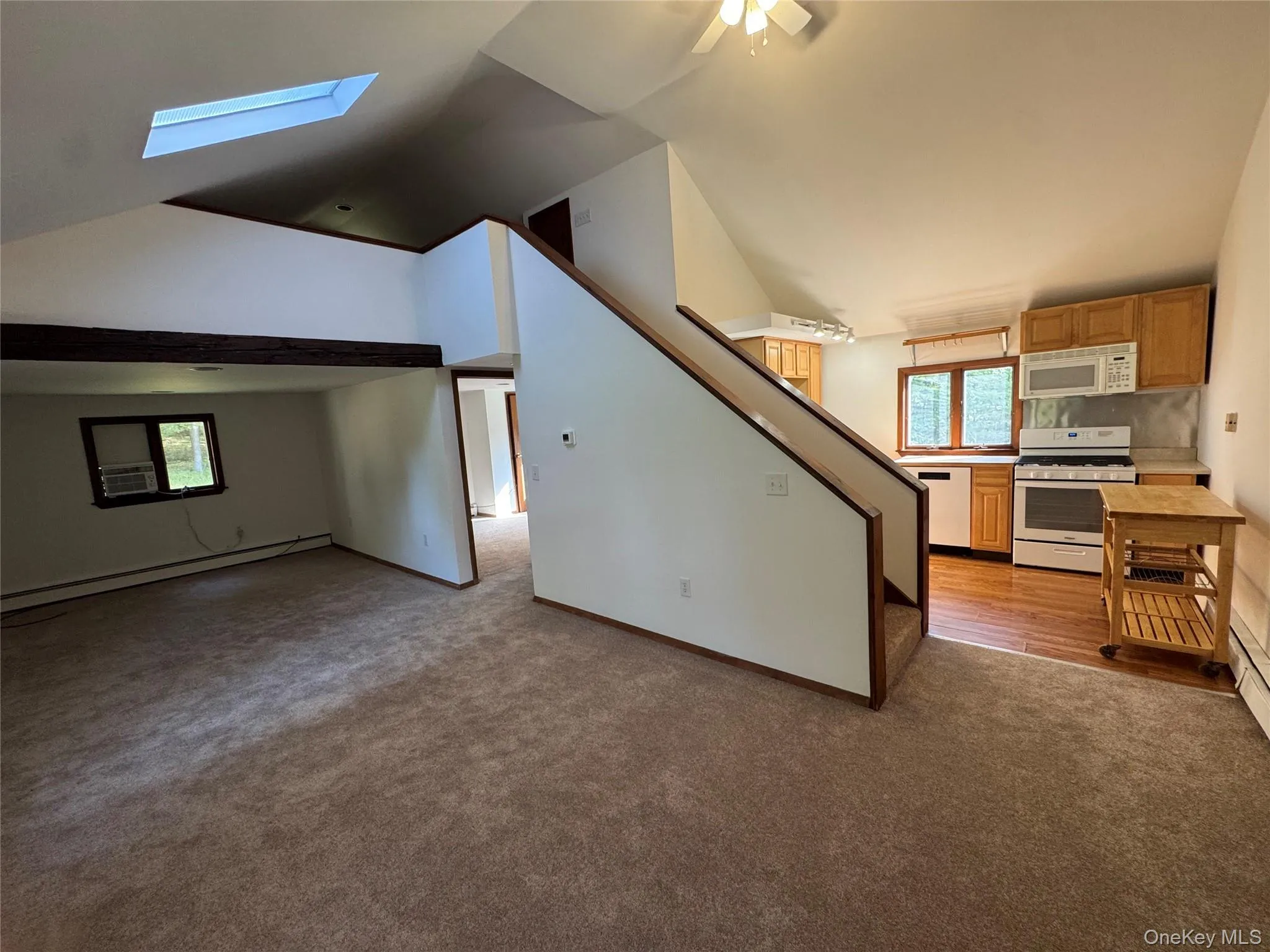 Kitchen featuring white appliances, a baseboard heating unit, dark carpet, a skylight, and lofted ceiling Kitchen featuring white appliances, a baseboard heating unit, dark carpet, a skylight, and lofted ceiling