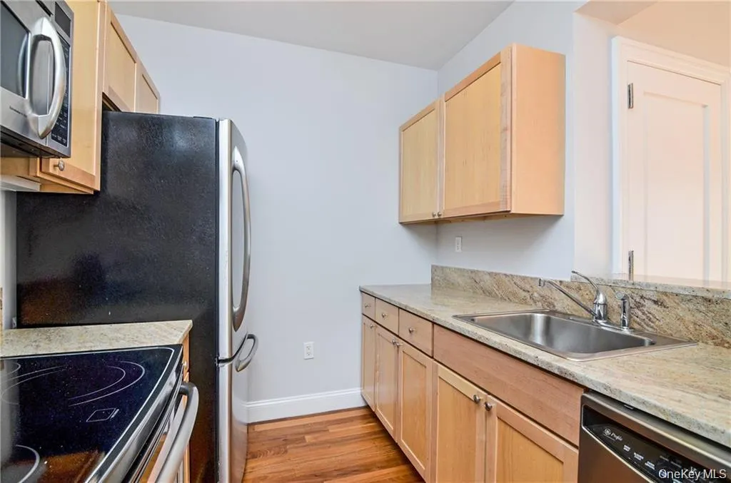 Kitchen featuring light brown cabinets, stainless steel appliances, light wood-type flooring, and light stone countertops Kitchen featuring light brown cabinets, stainless steel appliances, light wood-type flooring, and light stone countertops