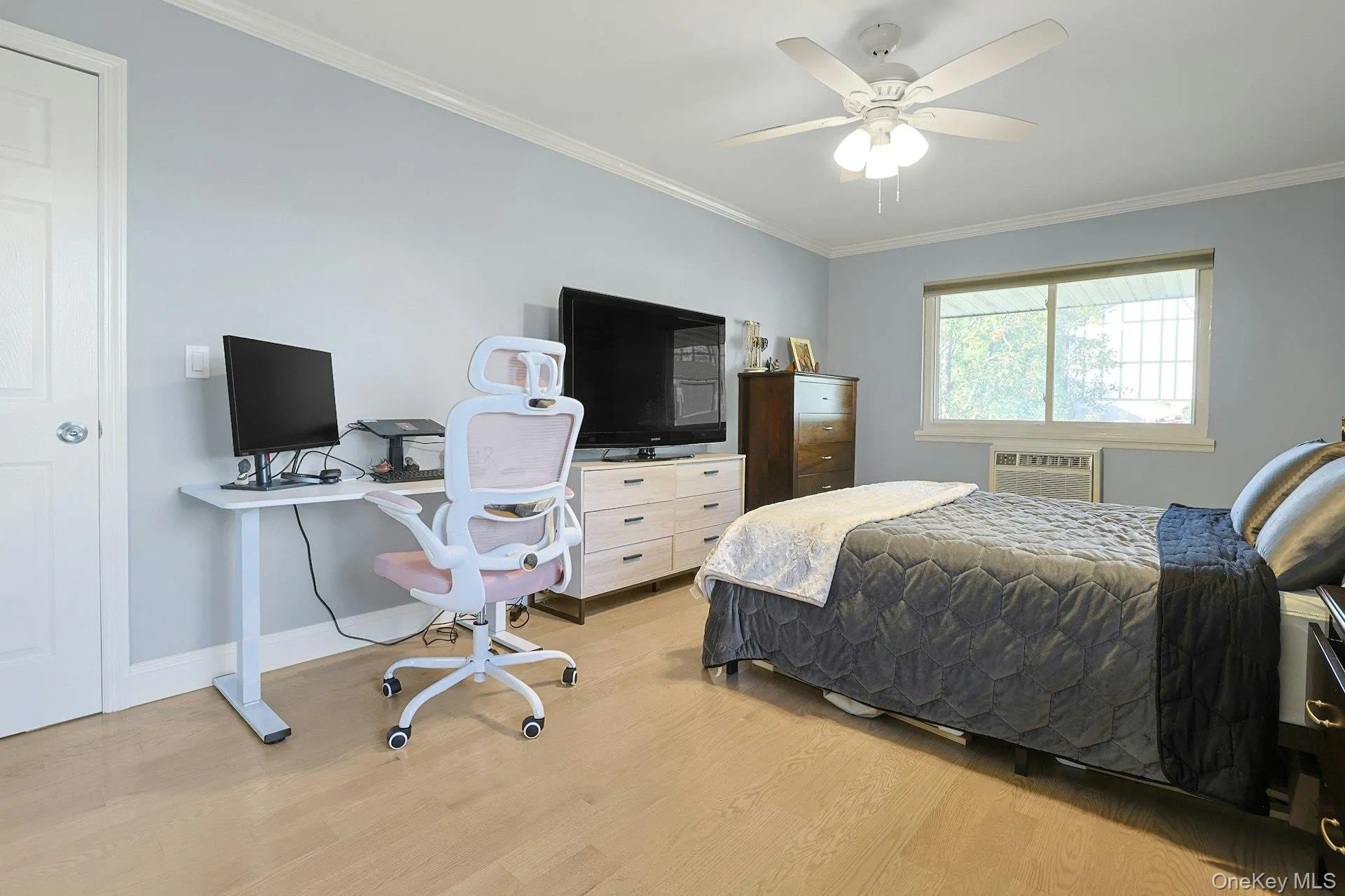 Bedroom with ornamental molding, light wood-style flooring, ceiling fan, a desk, and a wall mounted AC Bedroom with ornamental molding, light wood-style flooring, ceiling fan, a desk, and a wall mounted AC