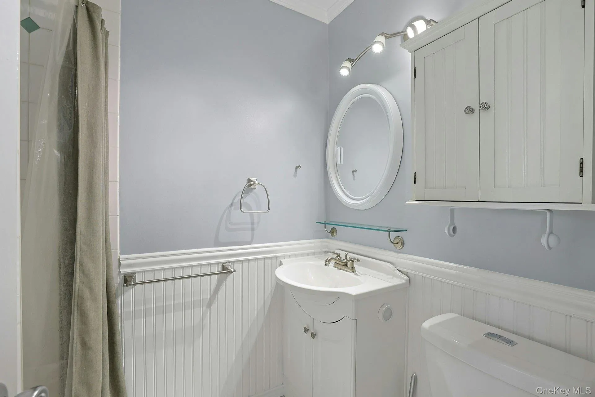 Full bath with vanity, a wainscoted wall, crown molding, and a shower with shower curtain Full bath with vanity, a wainscoted wall, crown molding, and a shower with shower curtain