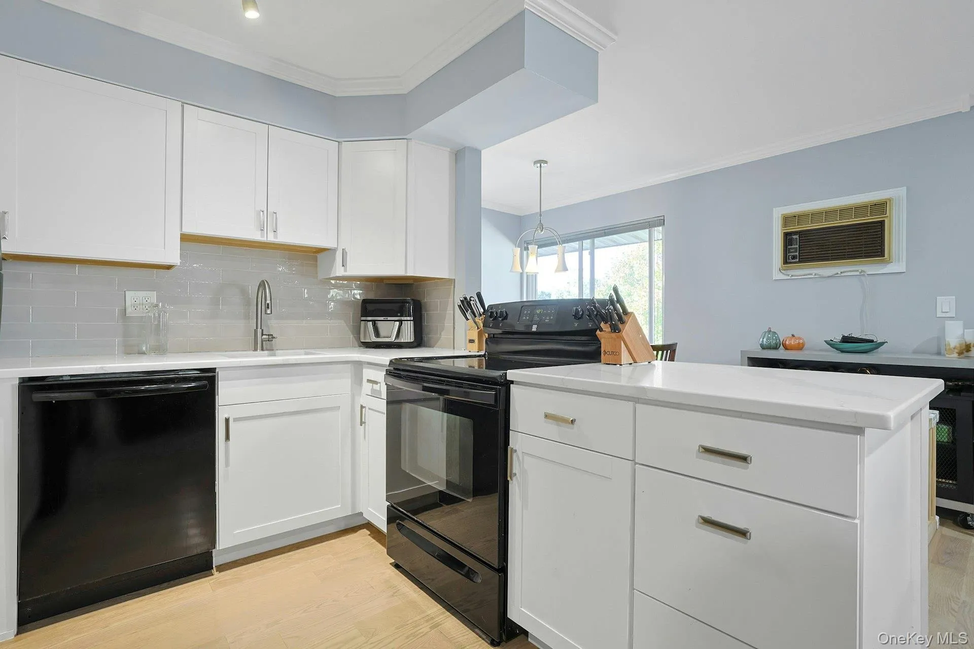 Kitchen with ornamental molding, white cabinets, black appliances, decorative backsplash, and light wood-type flooring Kitchen with ornamental molding, white cabinets, black appliances, decorative backsplash, and light wood-type flooring