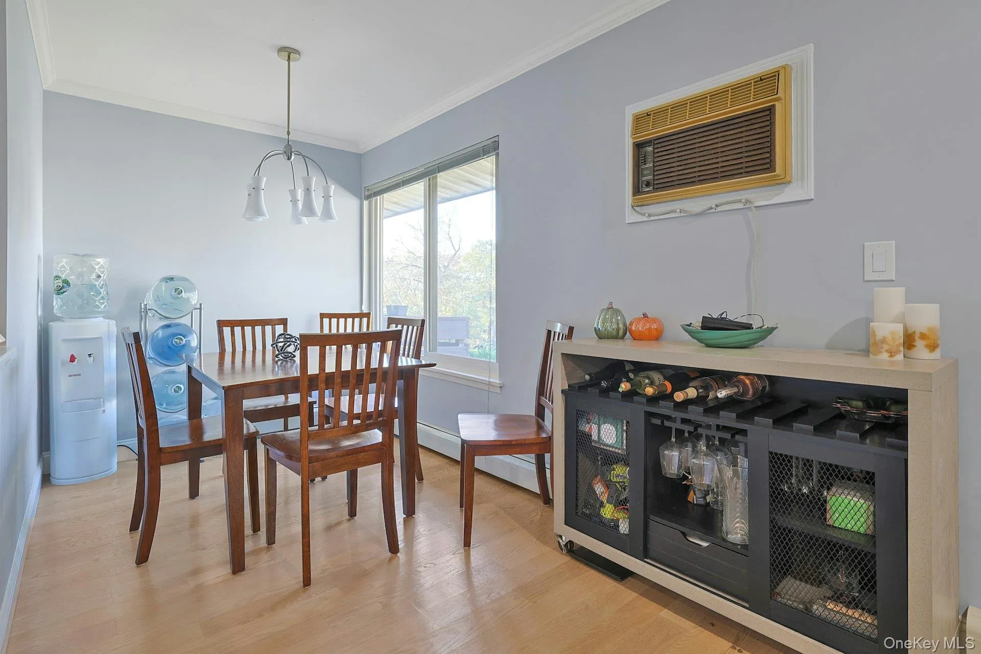 Dining space featuring light wood-style flooring, a wall unit AC, ornamental molding, and a chandelier Dining space featuring light wood-style flooring, a wall unit AC, ornamental molding, and a chandelier