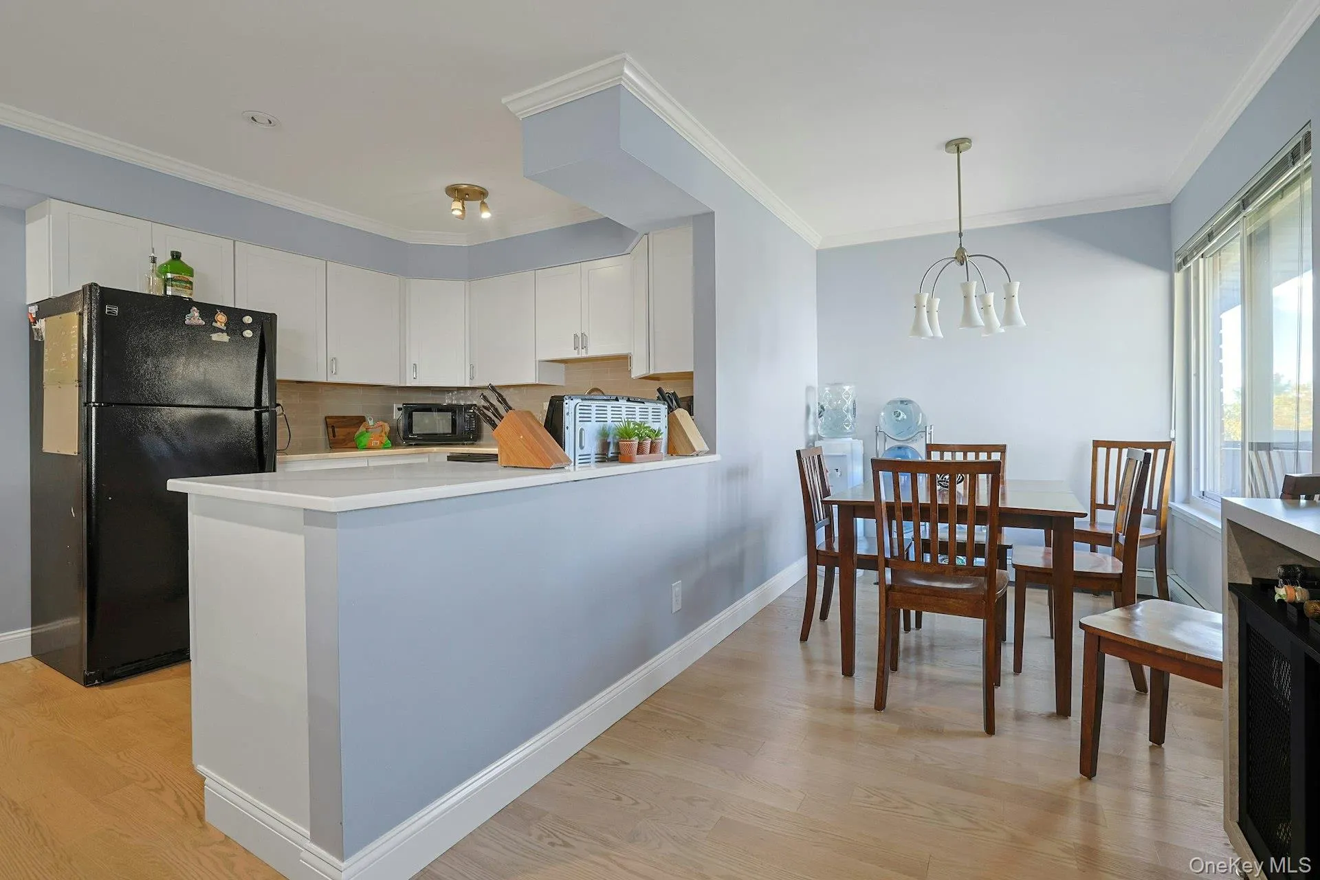 Kitchen with white cabinets, black appliances, ornamental molding, light countertops, and a chandelier Kitchen with white cabinets, black appliances, ornamental molding, light countertops, and a chandelier