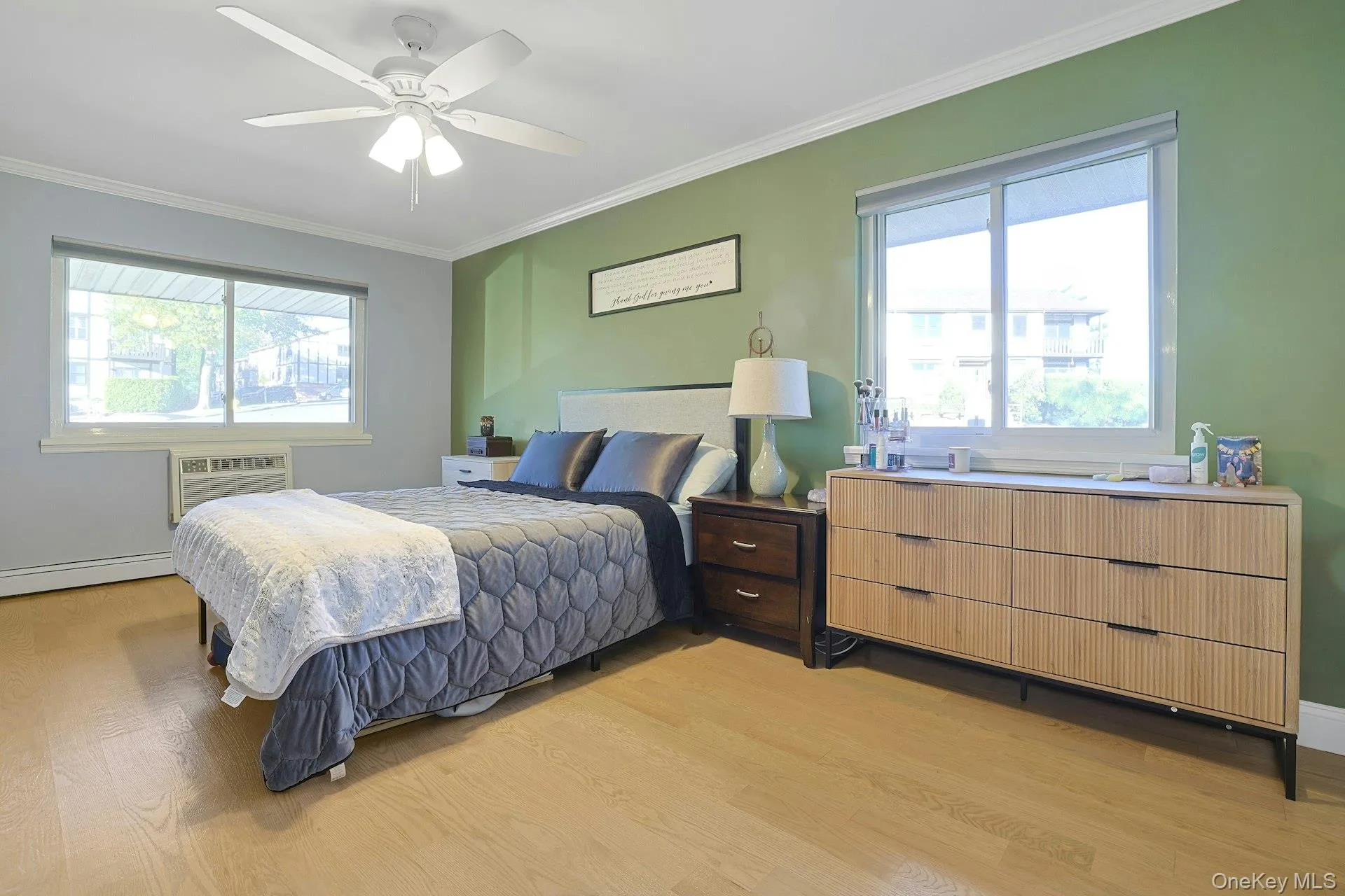 Bedroom featuring ornamental molding, multiple windows, light wood-style flooring, a ceiling fan, and a baseboard heating unit Bedroom featuring ornamental molding, multiple windows, light wood-style flooring, a ceiling fan, and a baseboard heating unit
