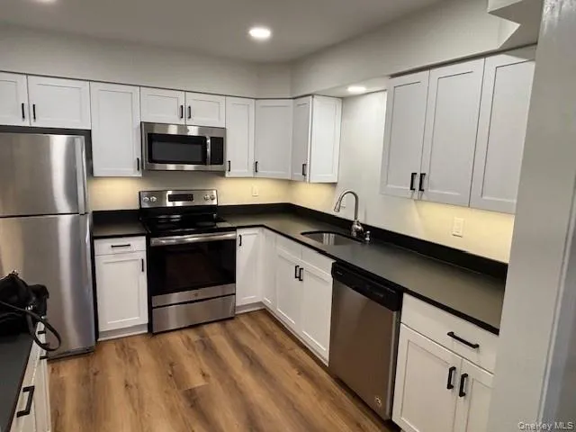 Kitchen featuring appliances with stainless steel finishes, white cabinetry, dark wood-style flooring, recessed lighting, and dark countertops Kitchen featuring appliances with stainless steel finishes, white cabinetry, dark wood-style flooring, recessed lighting, and dark countertops