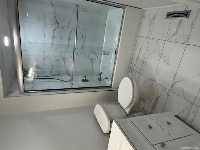 Full bathroom featuring vanity, shower / bath combination with glass door, and light marble finish floors Full bathroom featuring vanity, shower / bath combination with glass door, and light marble finish floors