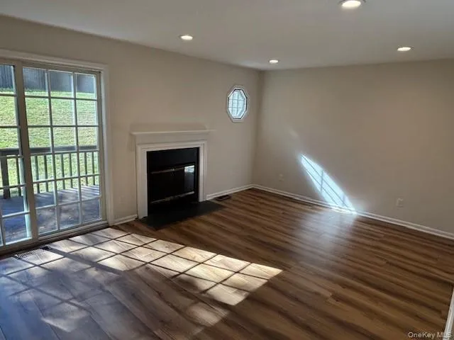 Unfurnished living room featuring a fireplace with flush hearth, dark wood-style flooring, and recessed lighting Unfurnished living room featuring a fireplace with flush hearth, dark wood-style flooring, and recessed lighting