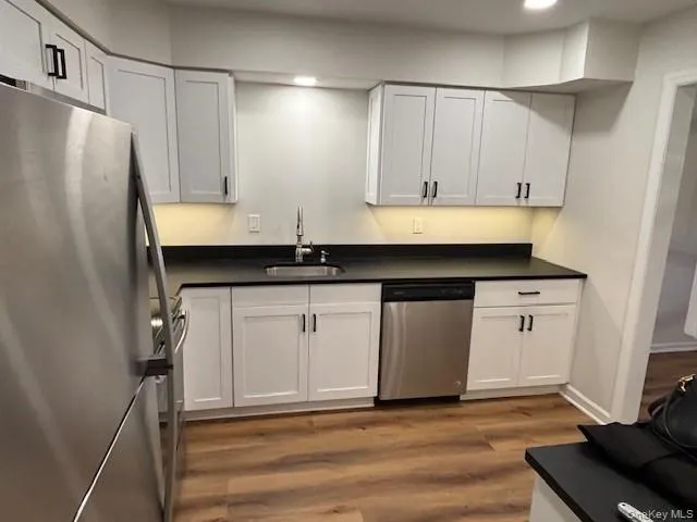 Kitchen with stainless steel appliances, dark wood-type flooring, dark countertops, white cabinetry, and recessed lighting Kitchen with stainless steel appliances, dark wood-type flooring, dark countertops, white cabinetry, and recessed lighting