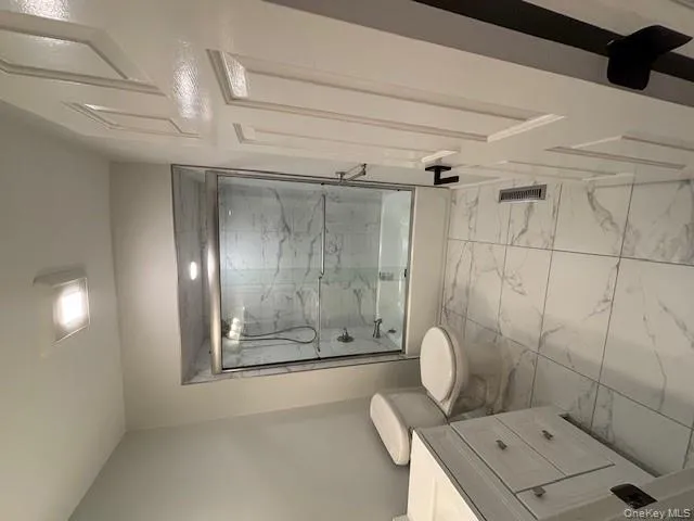 Bathroom with shower / bath combination with glass door, vanity, and light marble finish floors Bathroom with shower / bath combination with glass door, vanity, and light marble finish floors