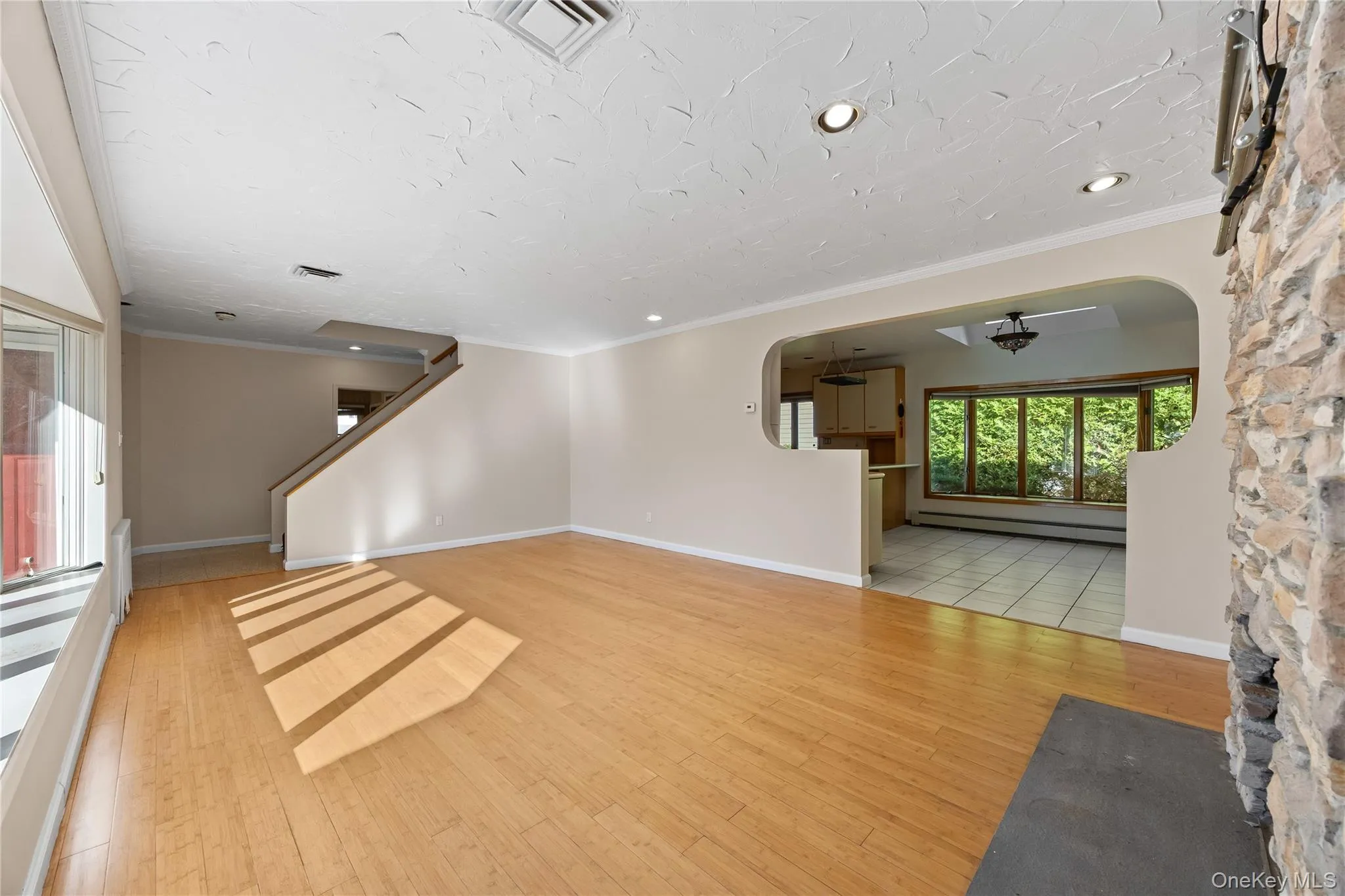 Unfurnished living room with crown molding, light wood-style floors, arched walkways, a baseboard heating unit, and recessed lighting Unfurnished living room with crown molding, light wood-style floors, arched walkways, a baseboard heating unit, and recessed lighting